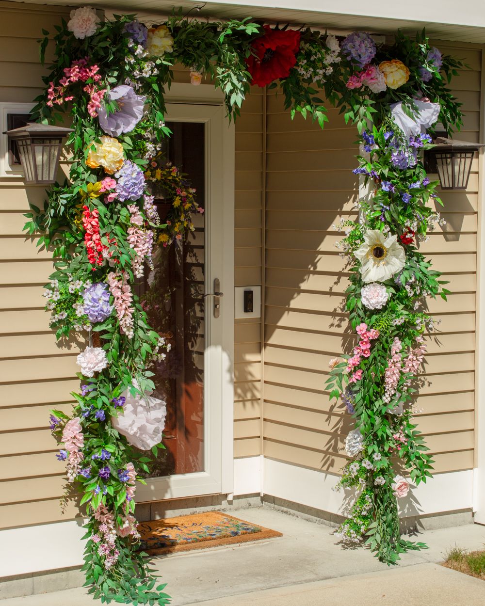Stunning multicolored flower arch framing a beige home's front door in full bloom.