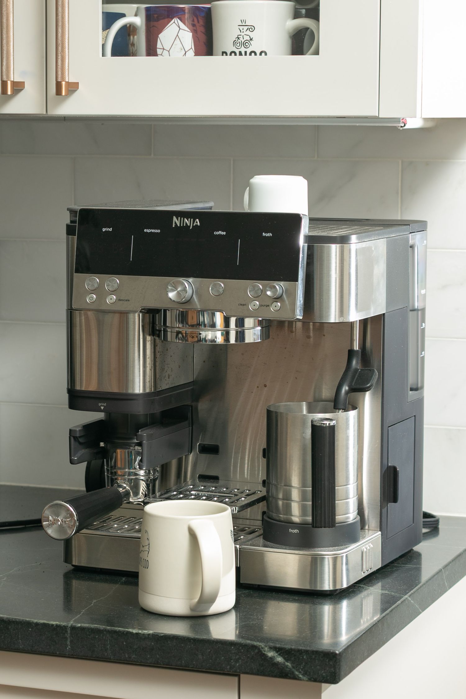 Ninja espresso and coffee maker on a dark marble kitchen countertop with a white mug.