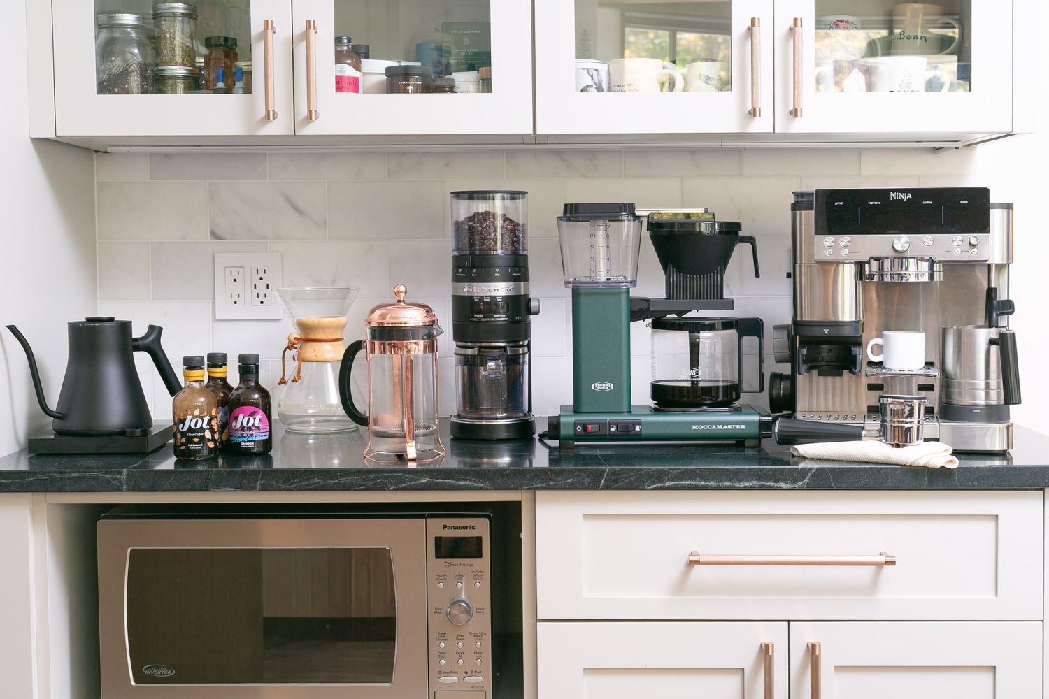 White kitchen counter with multiple coffee appliances including grinder, Moccamaster, and espresso machine.