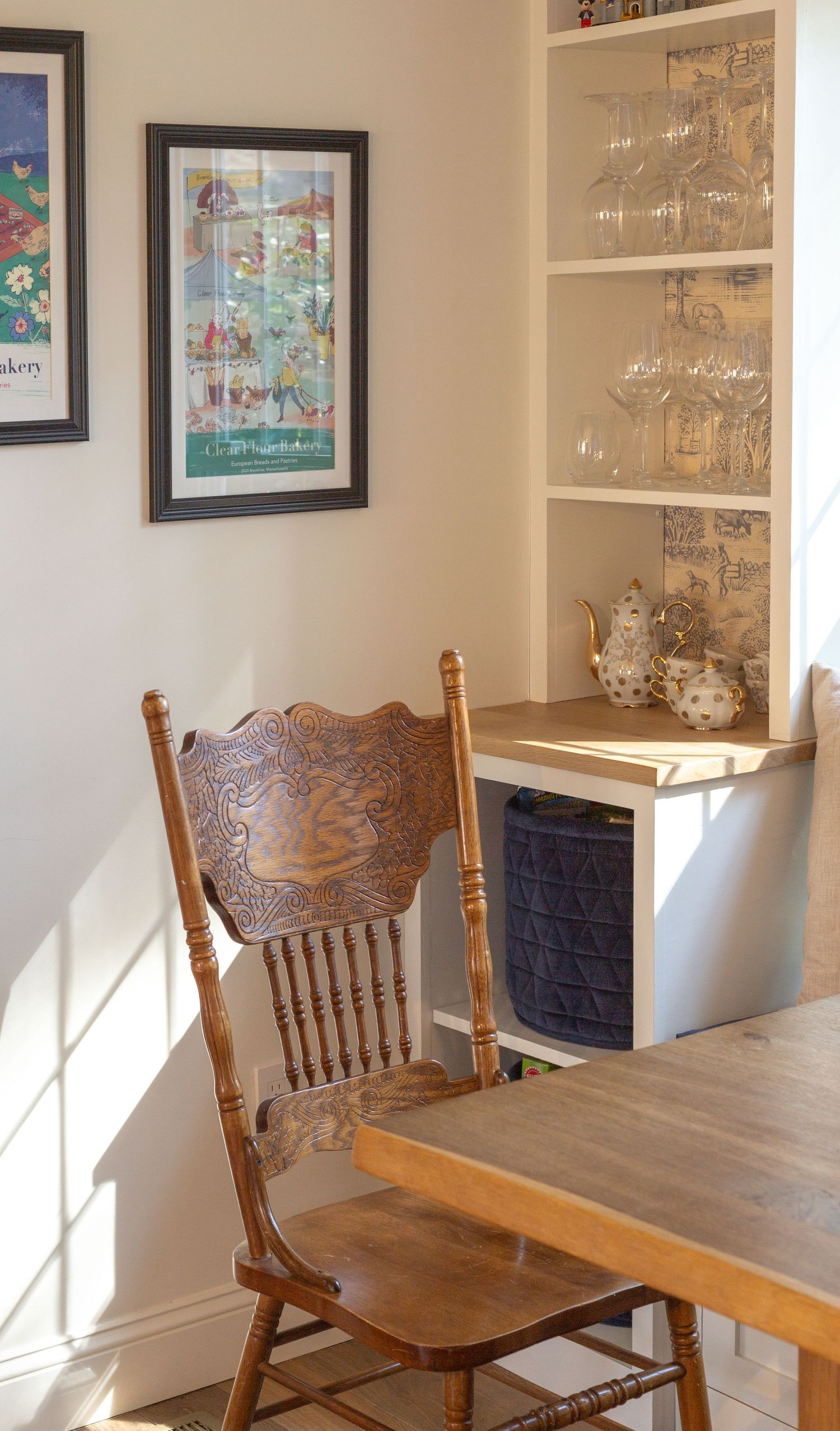 Vintage wooden chair at a dining table near a built-in shelf with glassware and teapot.