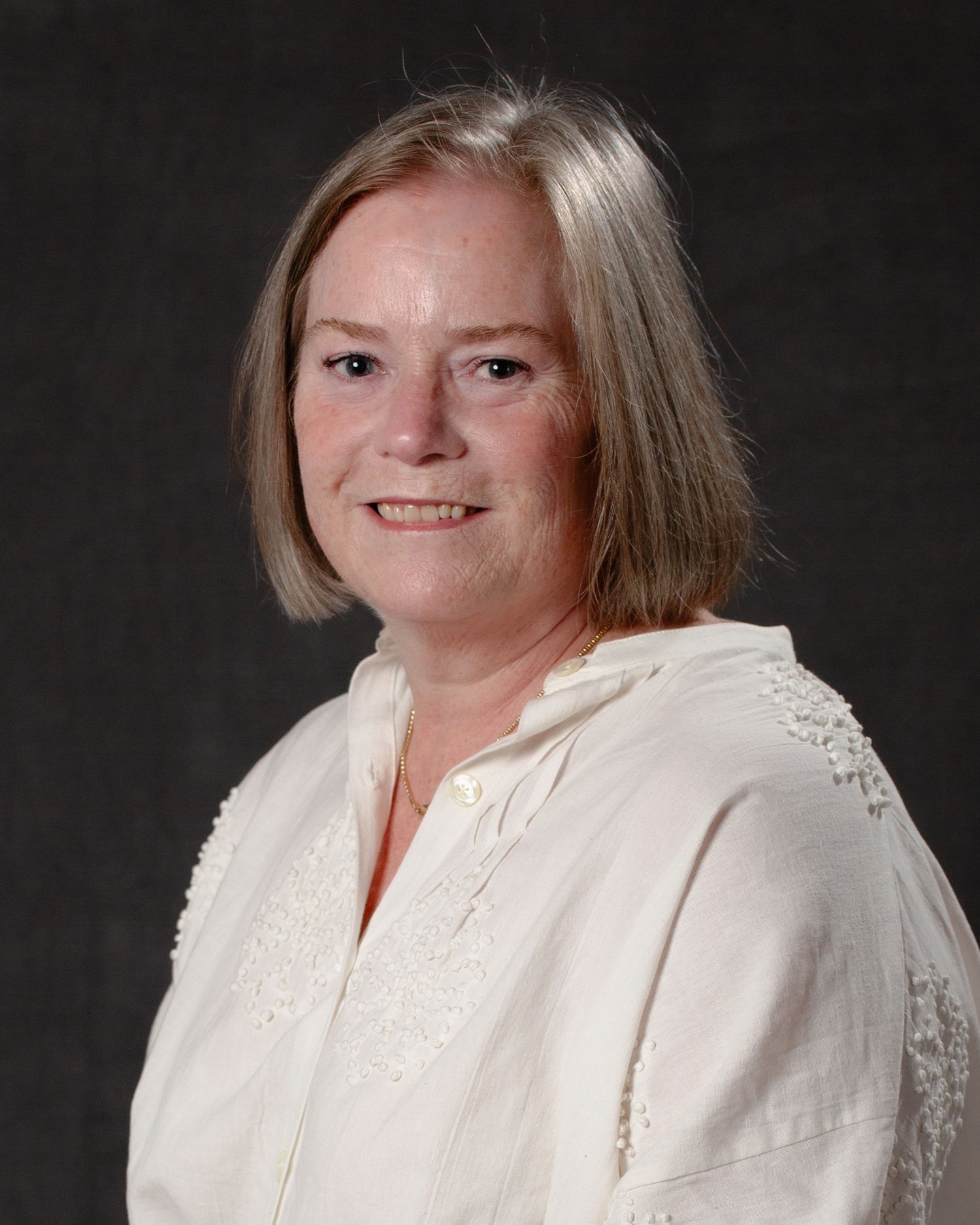 A smiling woman with shoulder-length blonde hair wearing a white blouse poses for a professional headshot.