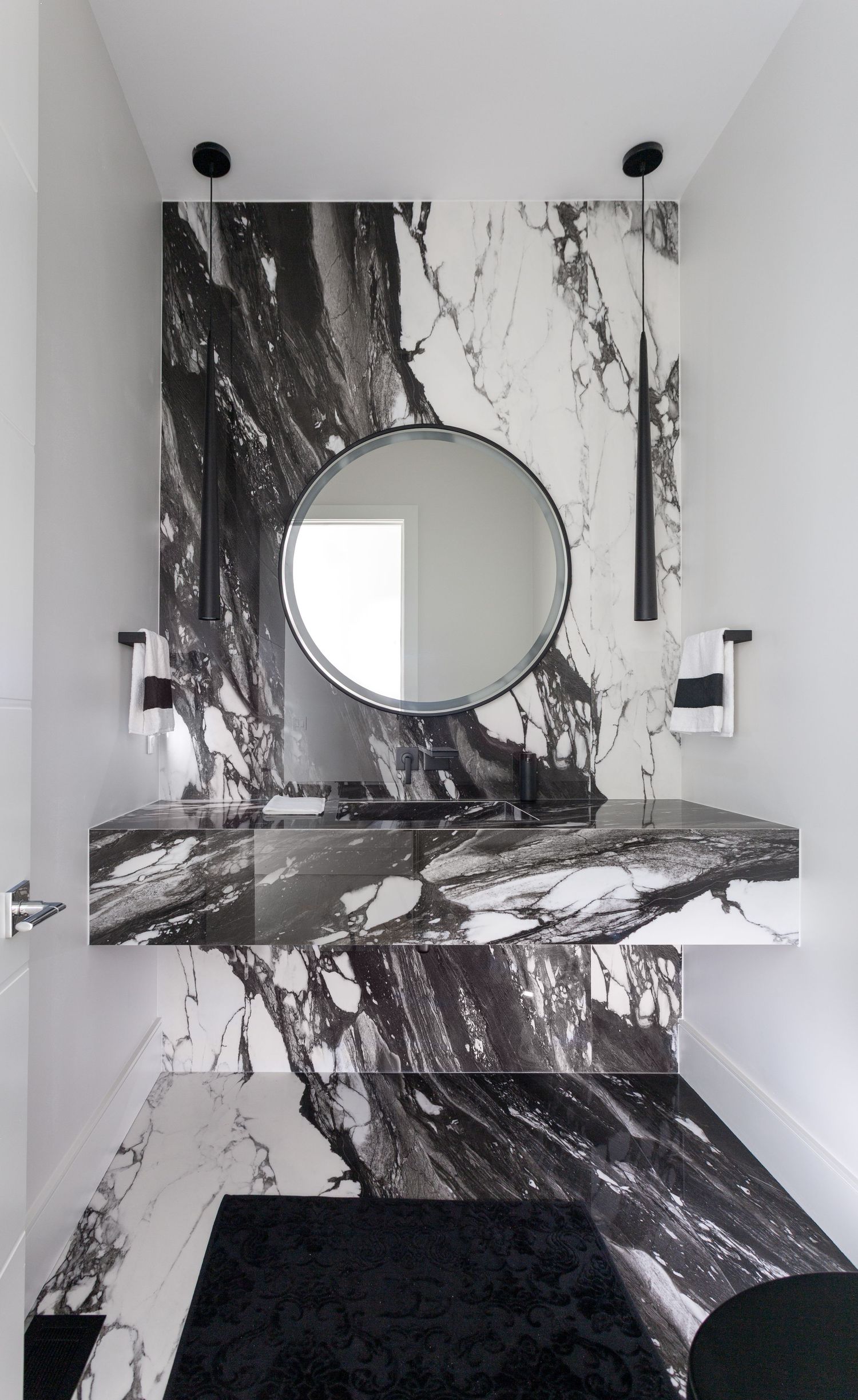 Luxurious powder room featuring dramatic black and white marble walls, floating vanity, and a round mirror with matte black accents.