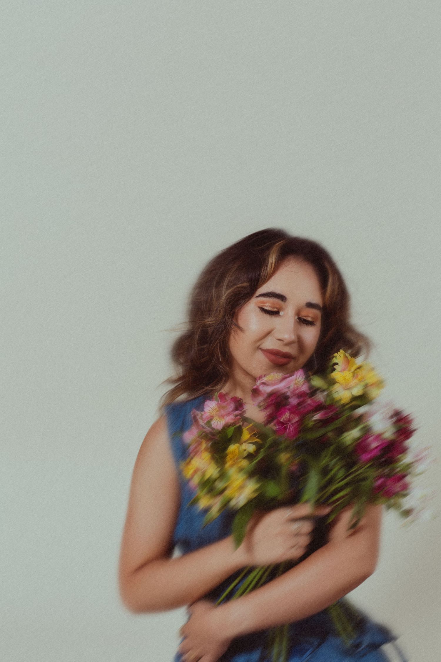 Young woman in a blue dress smiles while holding a bouquet of colorful pink and yellow flowers.
