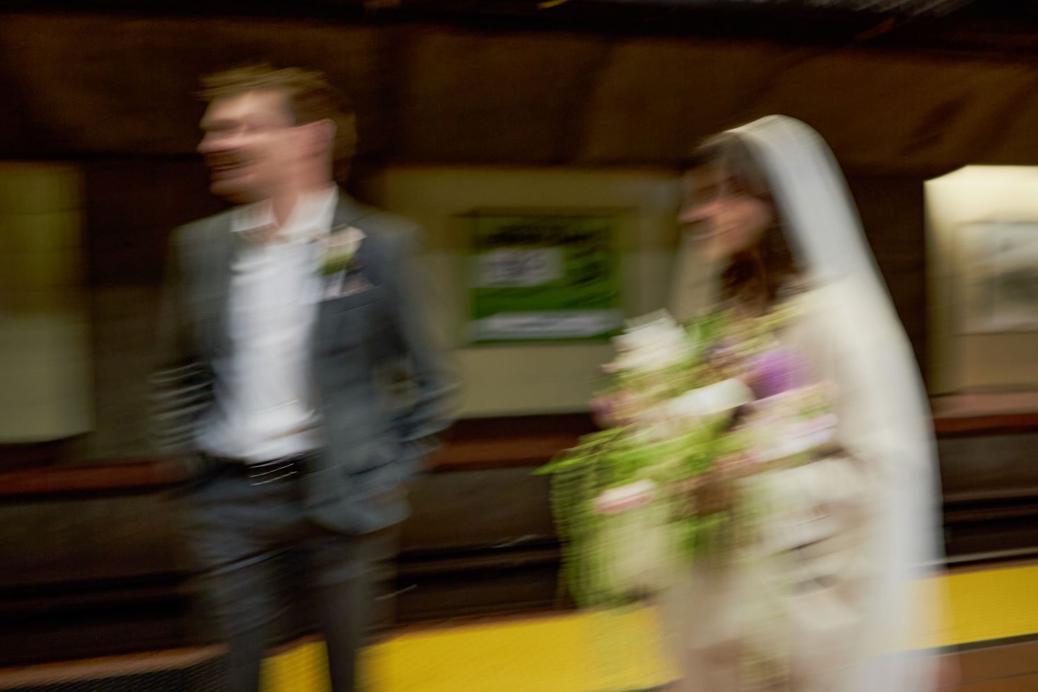 Blurred motion shot of a bride holding flowers and groom walking through a subway station on their wedding day.