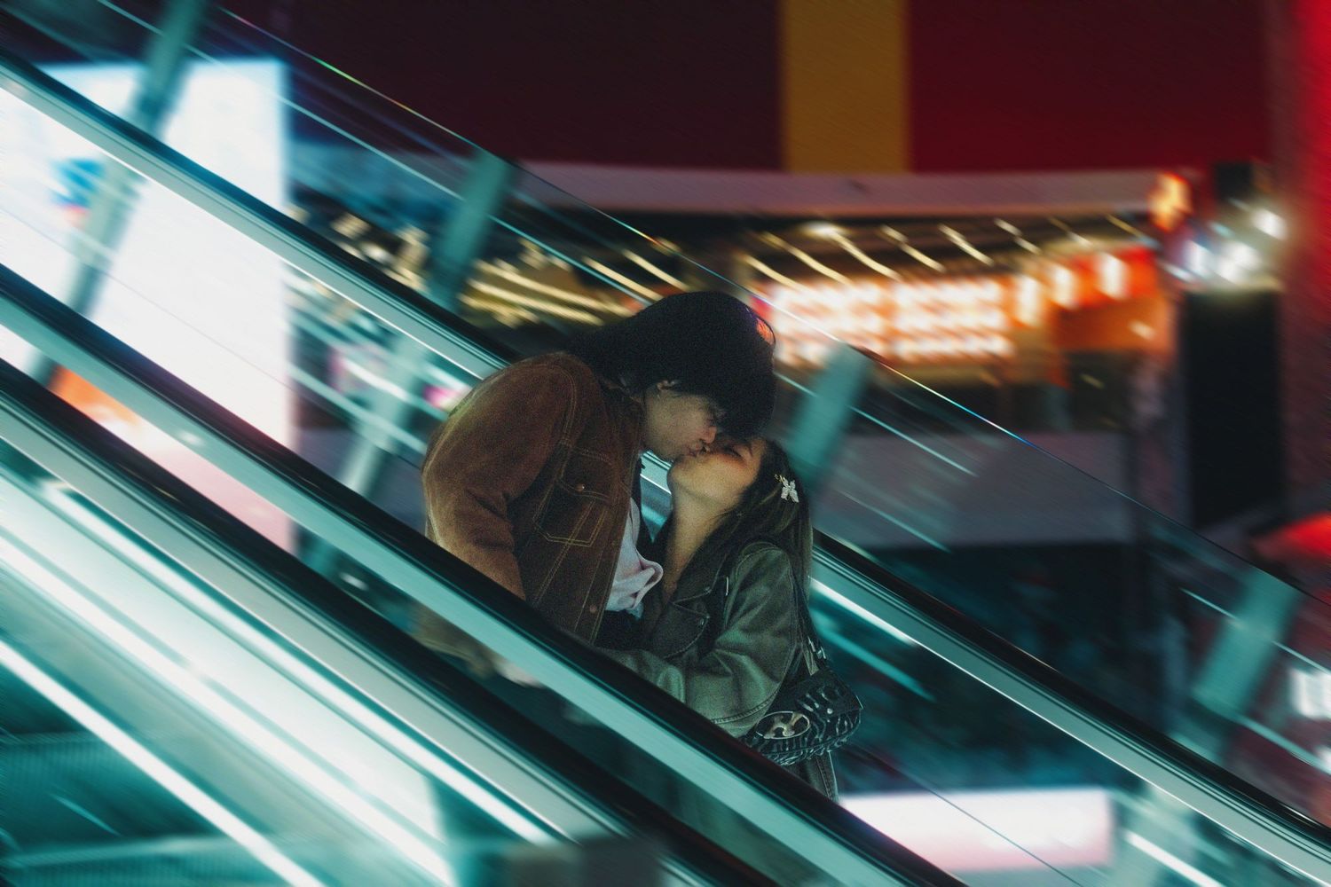 Woman on an escalator at night surrounded by colorful neon lights in an urban setting.