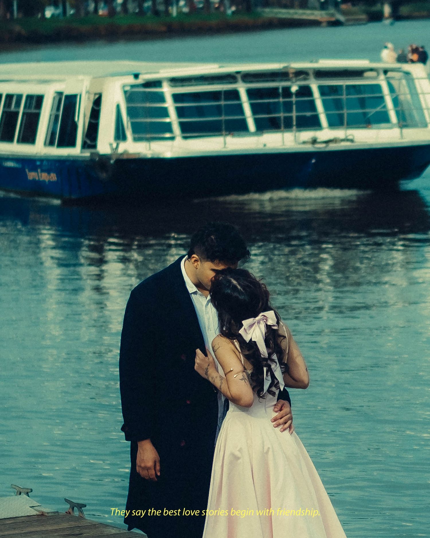 Couple sharing a romantic kiss on a waterfront dock with a blue boat behind them.