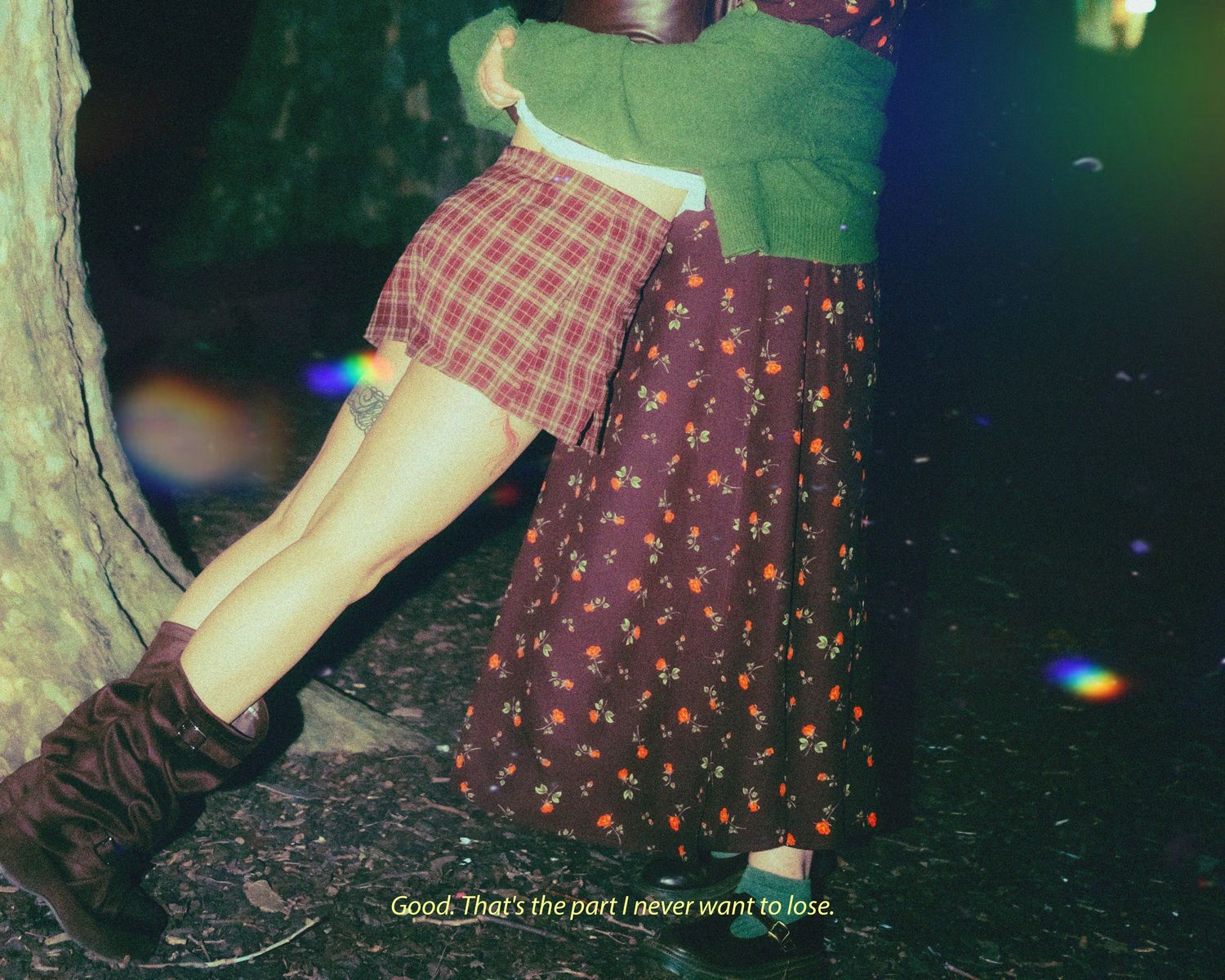 Two people embracing near a tree, wearing floral and plaid skirts with boots, in a dreamy outdoor setting.