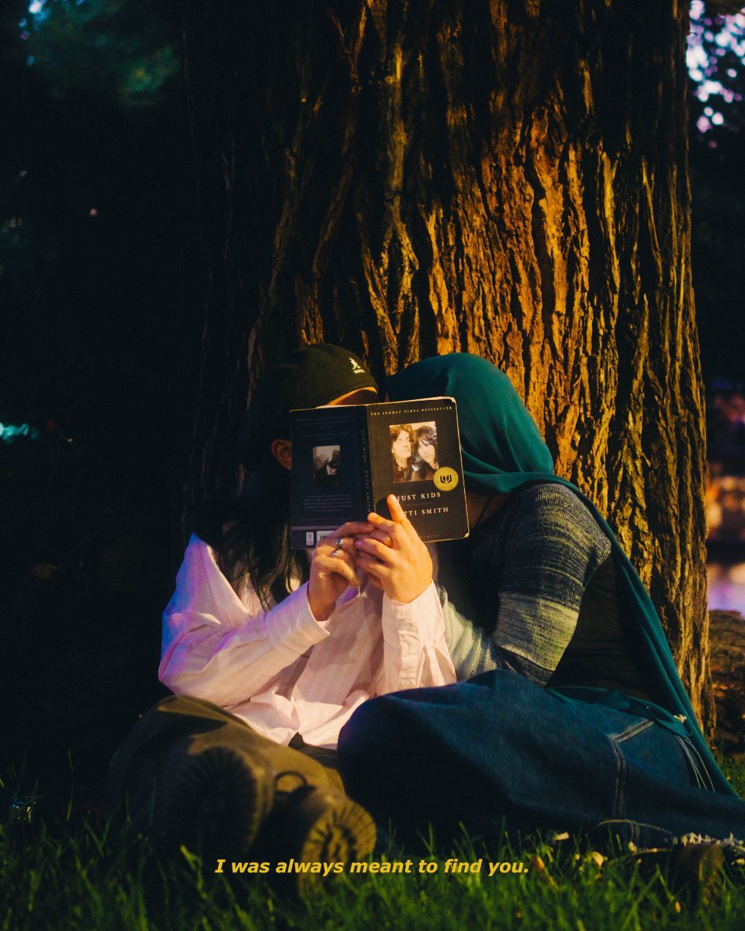 Couple sitting against a tree at night sharing a book with warm golden light.