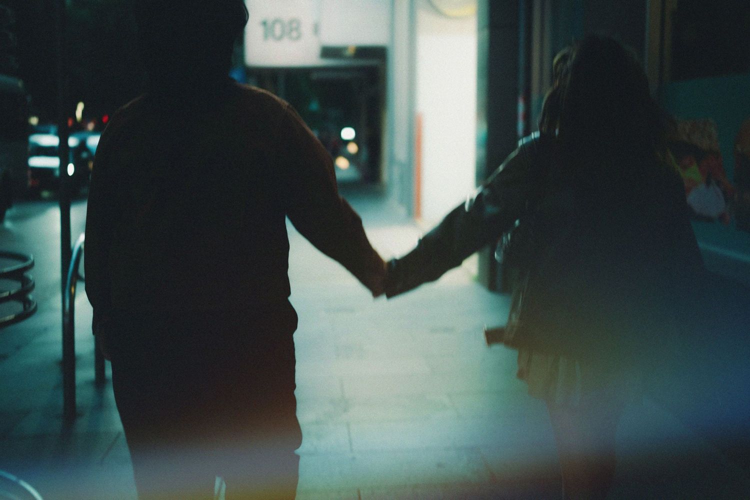 Couple holding hands silhouetted in a dimly lit urban alleyway at night.
