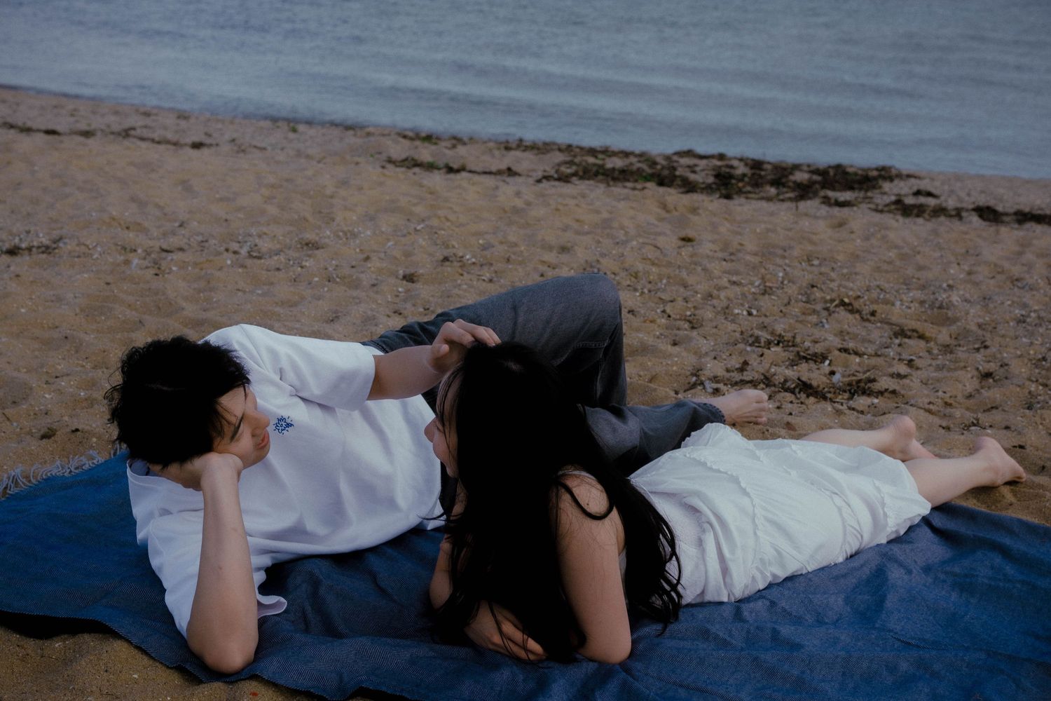 Romantic couple lying together on a blanket on a sandy beach near the water.