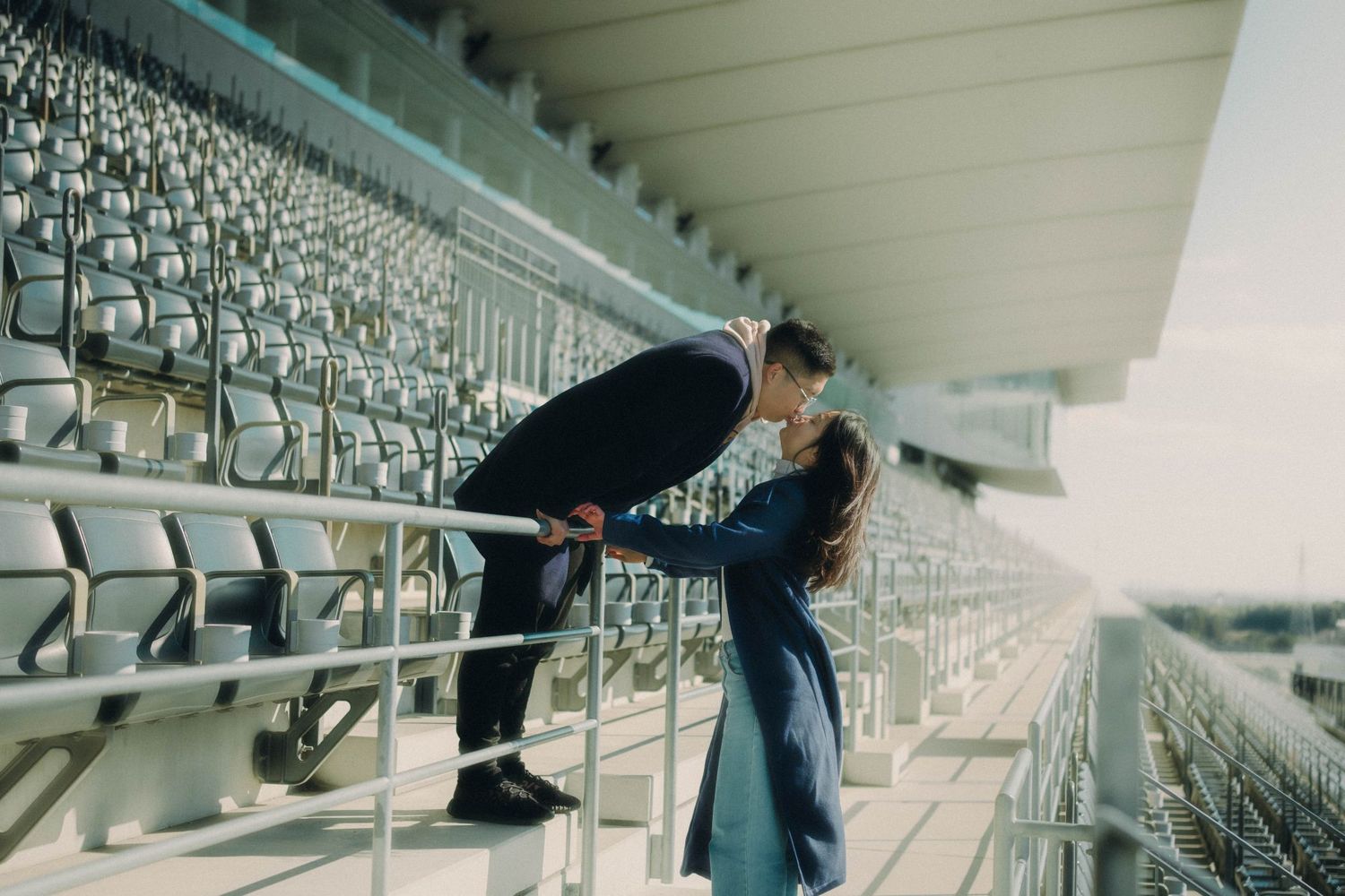 Couple sharing a kiss on stadium bleacher railings outdoors.