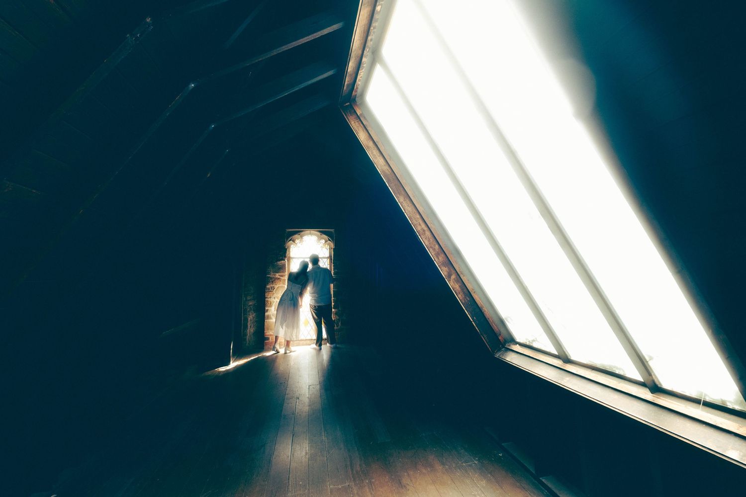 Silhouette of a person walking toward bright light at end of dark wooden hallway with dramatic angled windows.