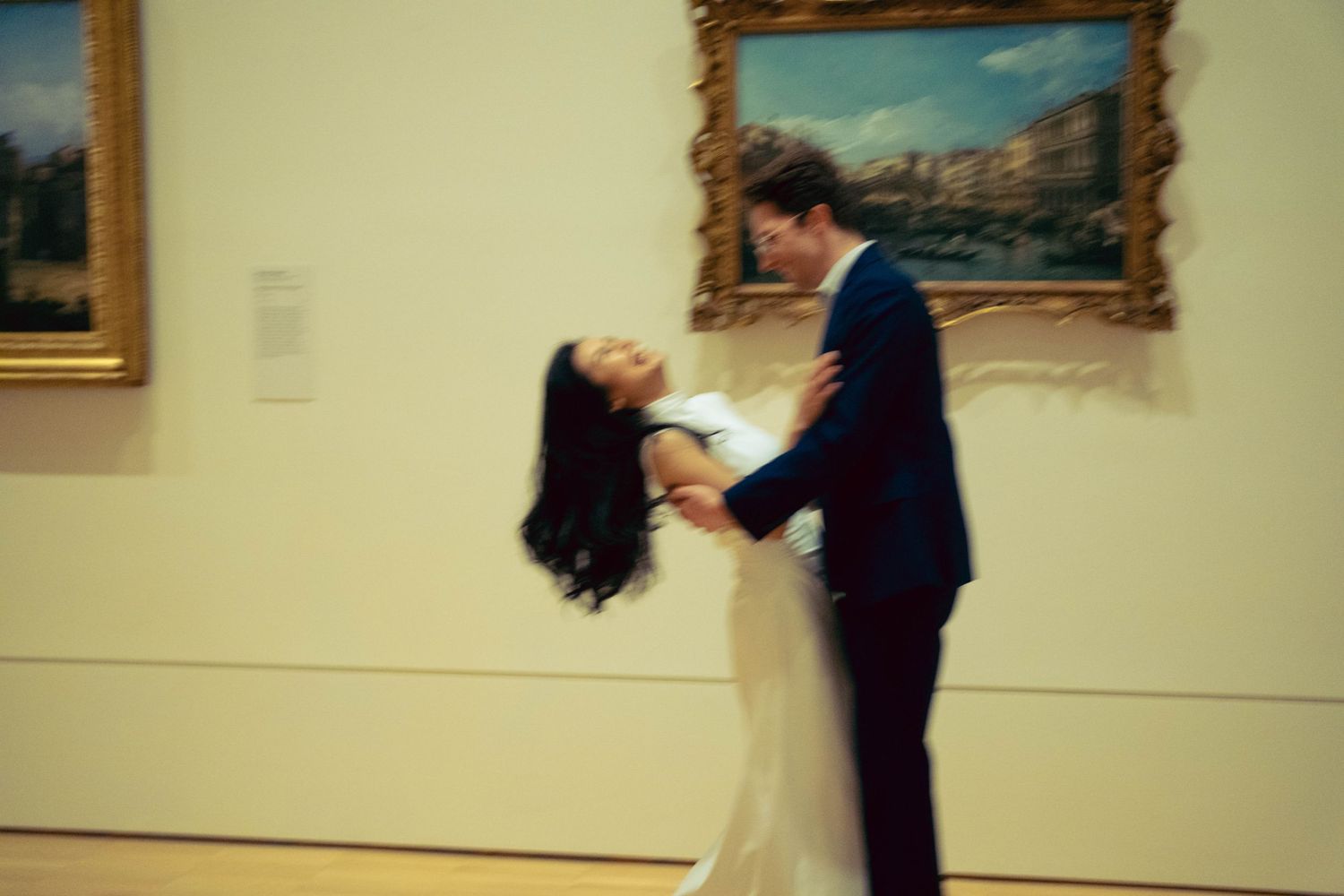 Couple dancing and spinning in motion blur inside elegant art gallery.