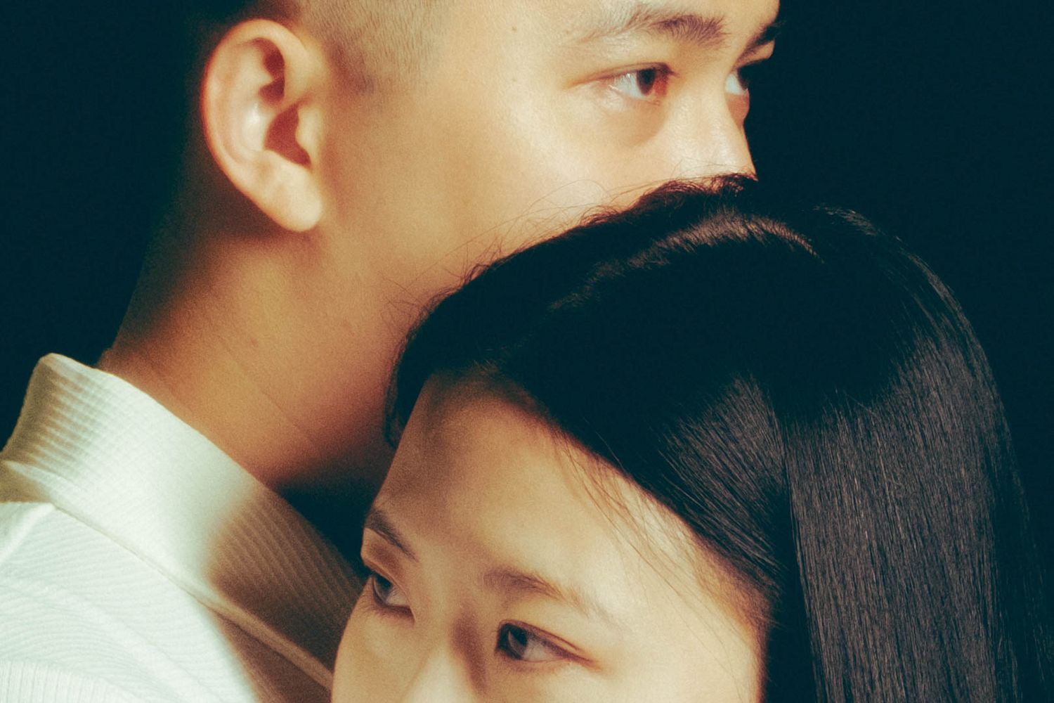A tender close-up of an Asian couple embracing, the man resting his chin on the woman's head affectionately.