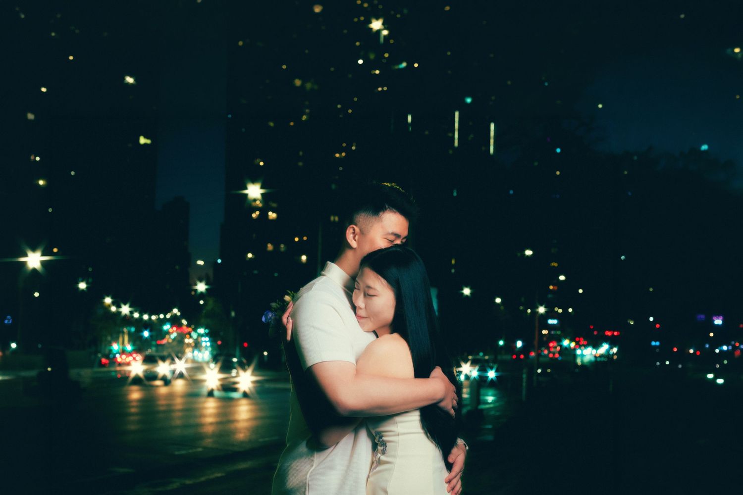Couple embracing romantically at night with bokeh city lights glowing in the dark background.