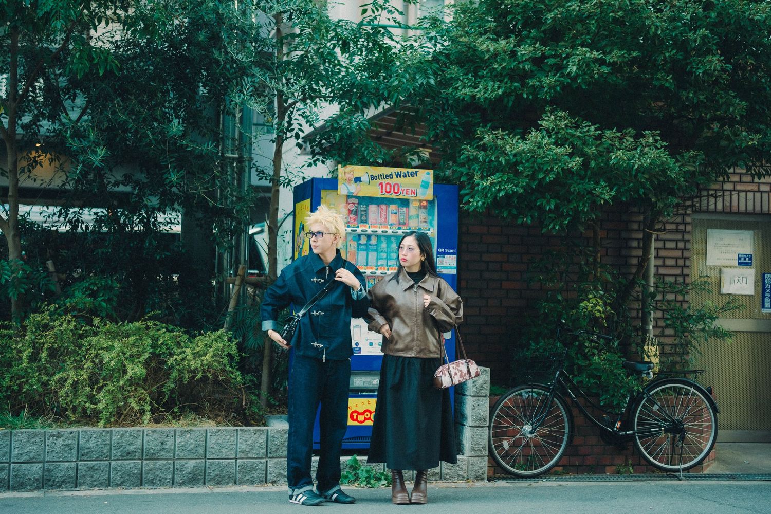 Two friends with blonde hair standing together on a quiet urban street near a vending machine.