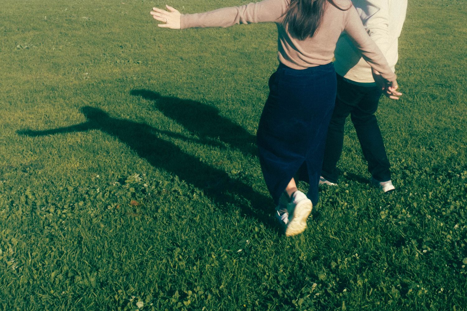 Two people walking on green grass field casting long shadows in warm sunlight.