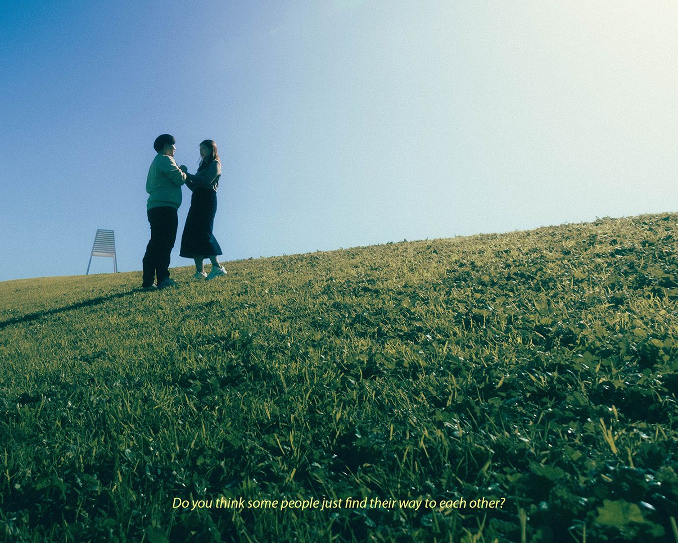 Two people standing on a lush green hill silhouetted against a clear blue sky, with text overlay on the image.
