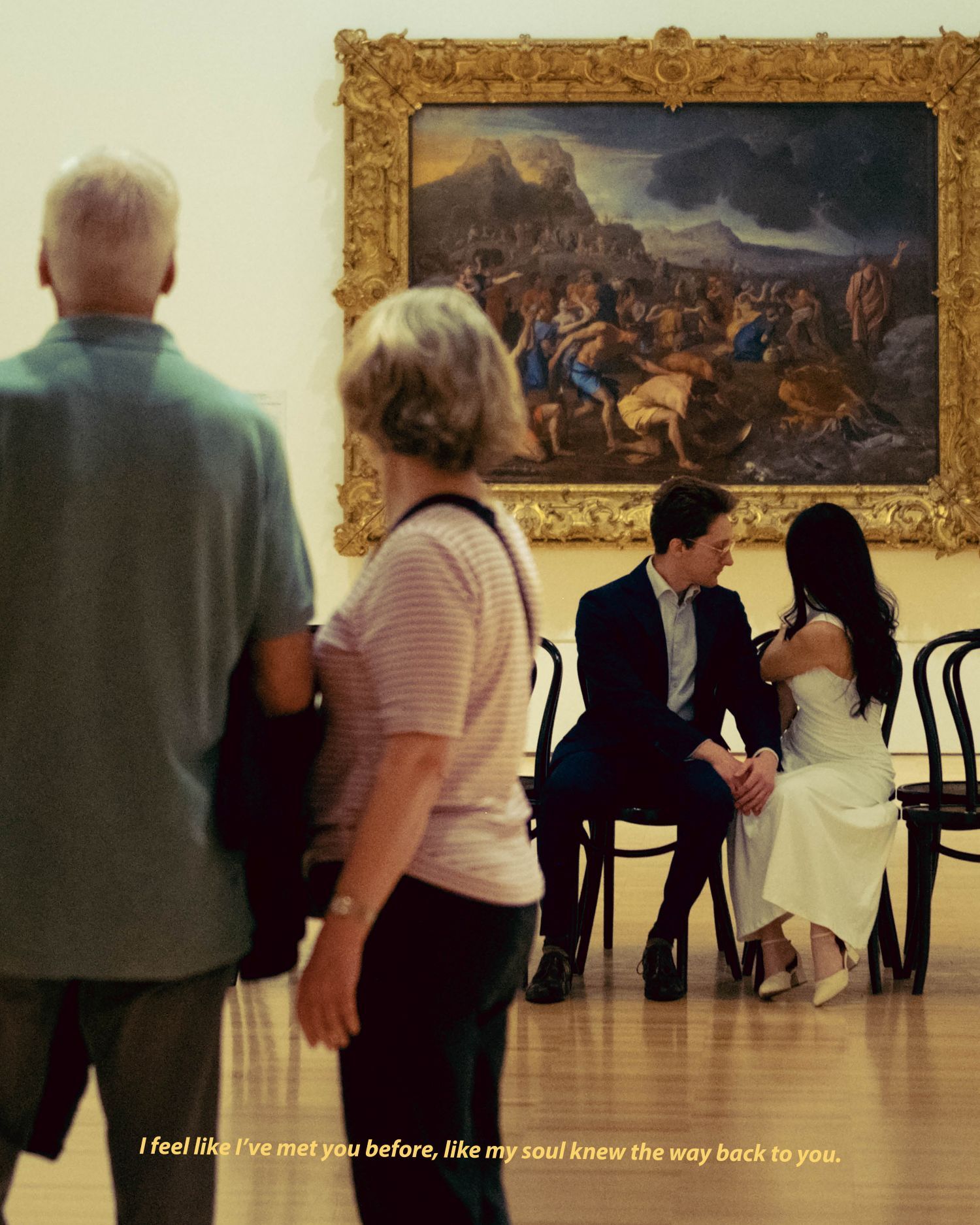 Couple sitting intimately in a museum gallery while visitors walk past a large painting.