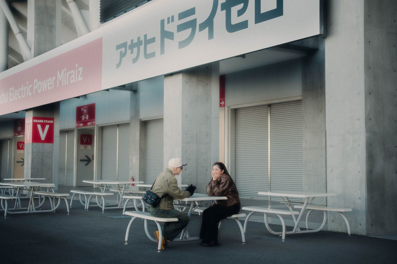 Two people sitting at outdoor tables near Japanese storefront.