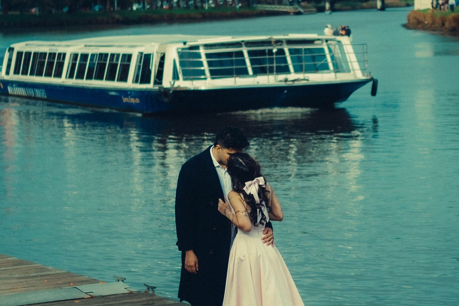 Couple kissing on dock with blue tourist boat on turquoise water behind them.