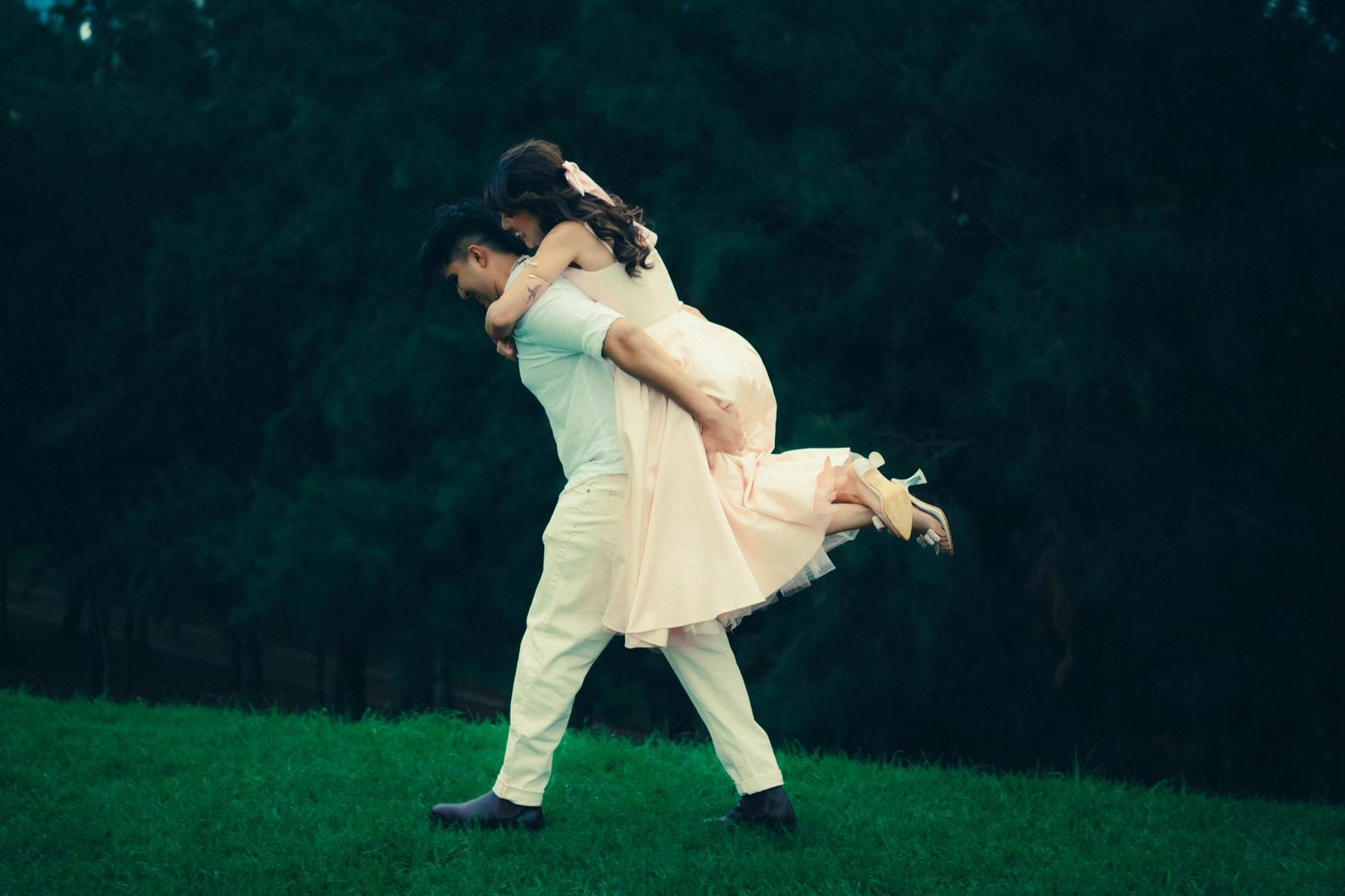 Man lifting woman in white dress on a lush green lawn.
