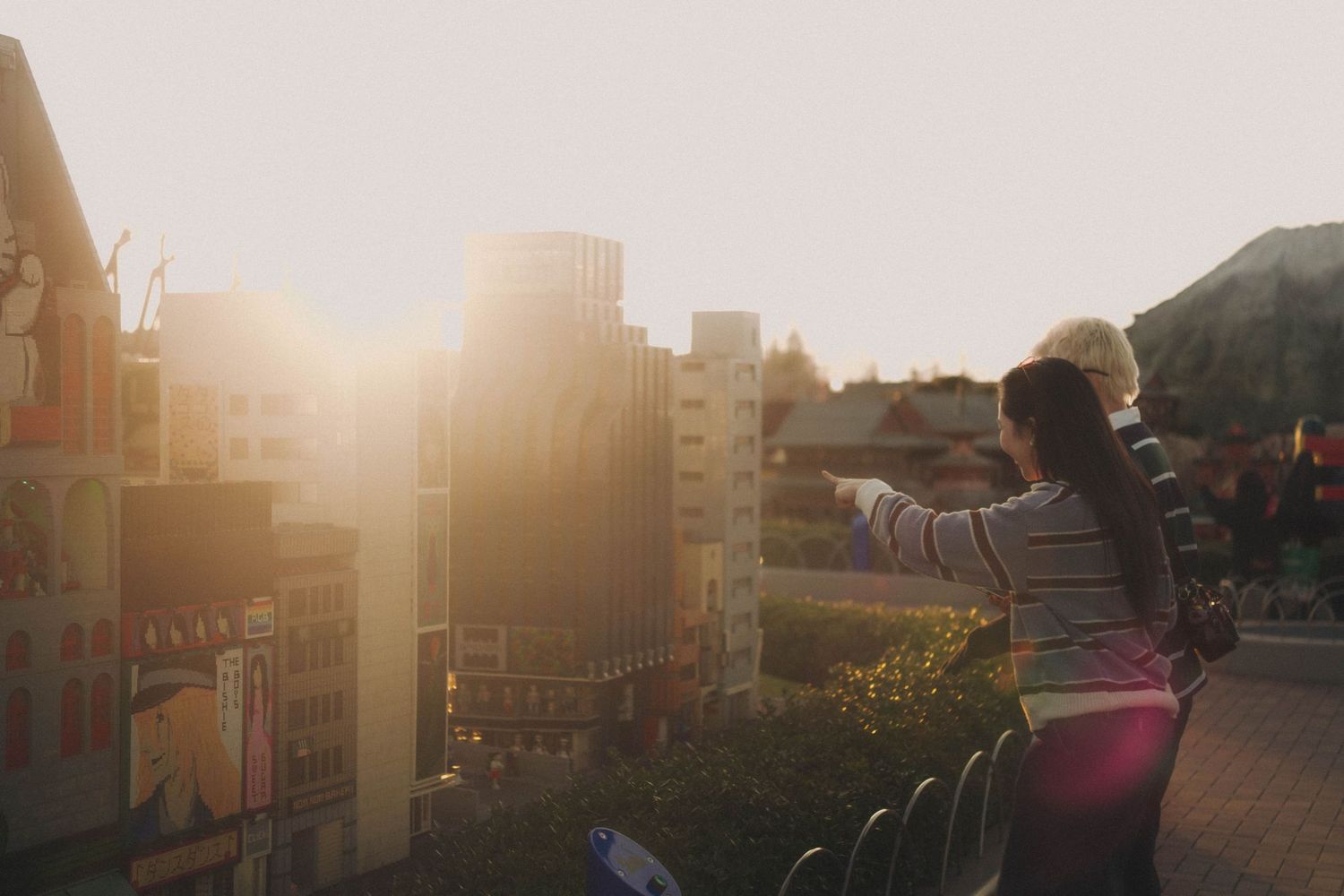 Girl pointing at miniature city models during golden hour sunset.