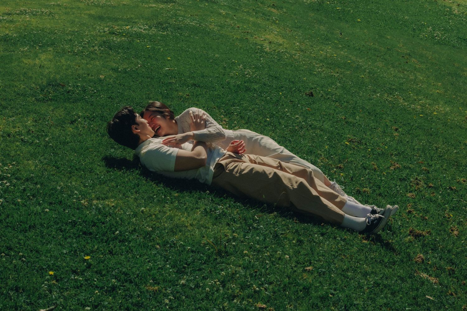 Couple lying together cuddling on green grass in a peaceful outdoor setting.