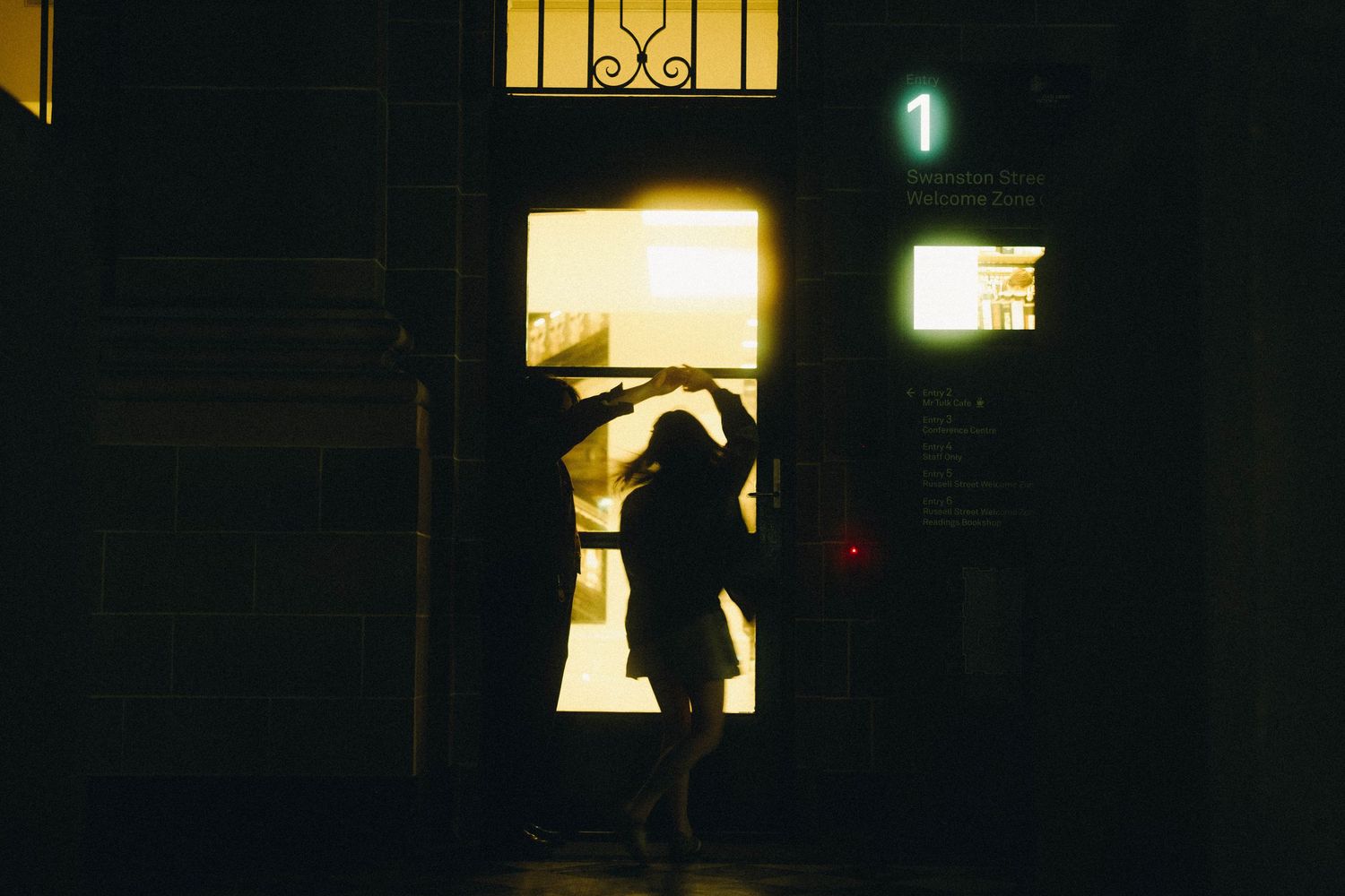 Silhouette of person dancing in glowing doorway at night beside number one sign.