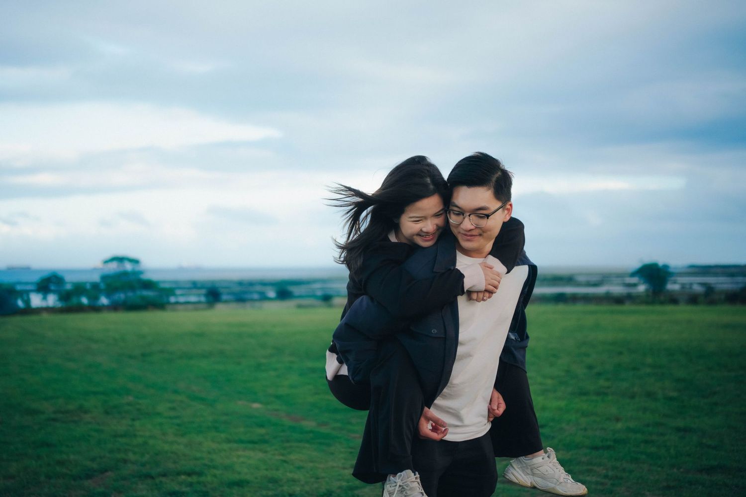 Man giving woman a piggyback ride in an open green field.