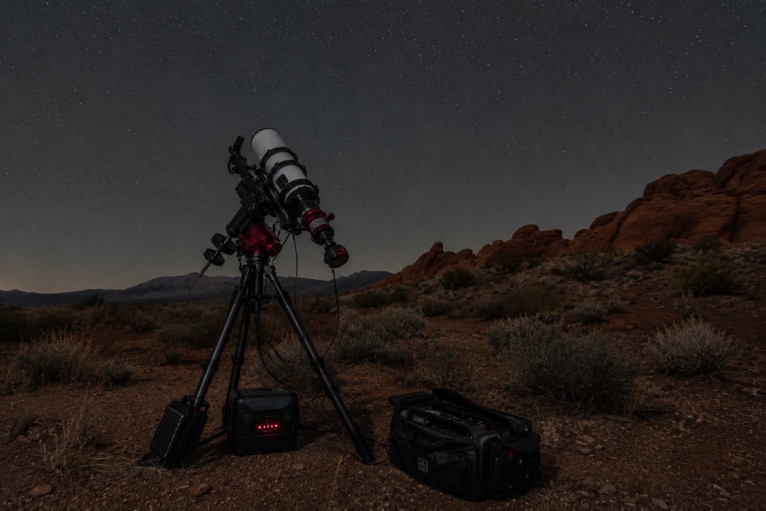 Telescope on tripod set up for astrophotography in desert landscape under clear night sky with rocky formations.