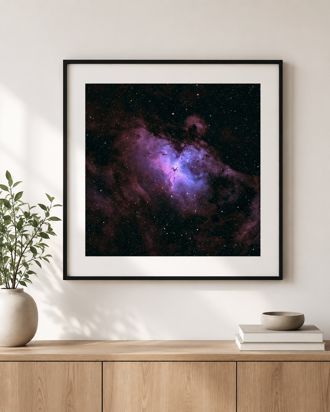 Framed print of the Eagle Nebula with vivid purple and blue cosmic clouds, displayed above a wooden sideboard in a modern interior.