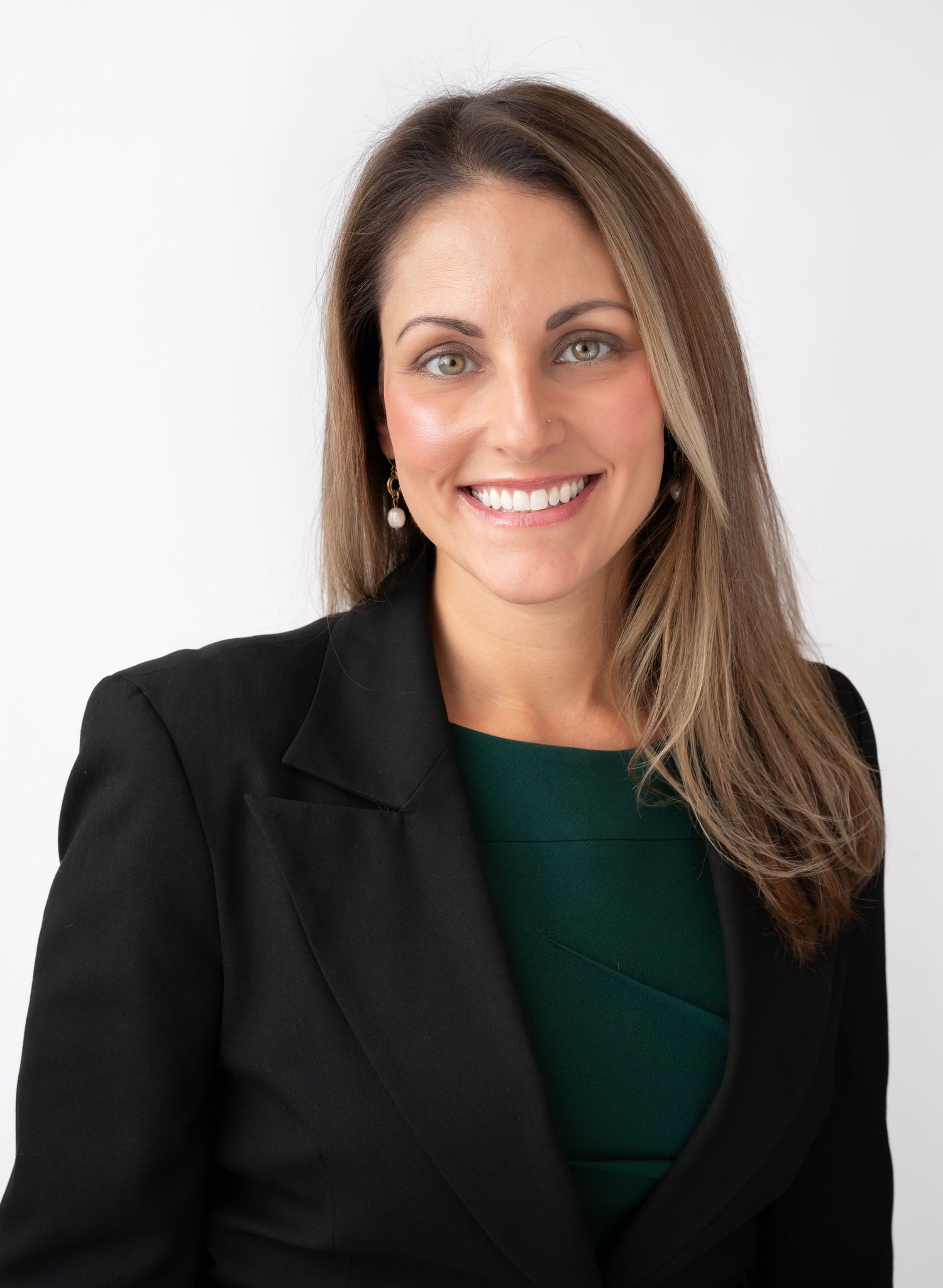 Professional headshot of a smiling woman with long brown hair wearing a black blazer and green top.