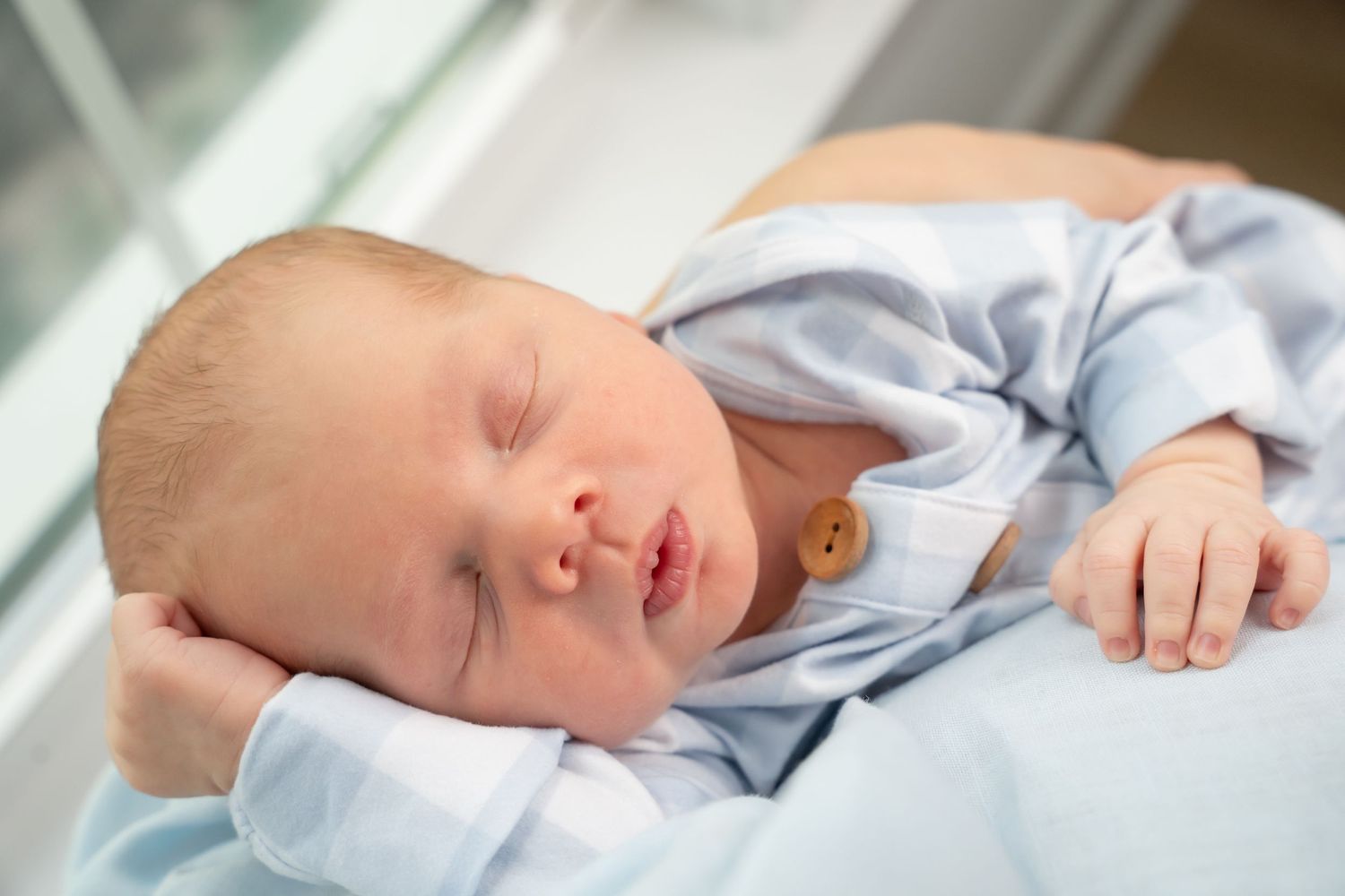 Peaceful sleeping newborn in light blue clothing against white bedding.