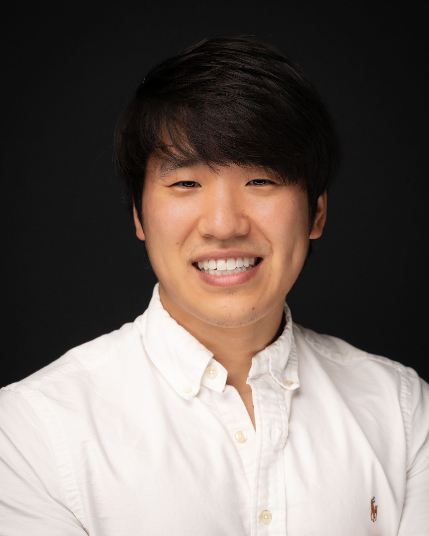 Professional headshot portrait of someone wearing a white button-down shirt against a dark background.