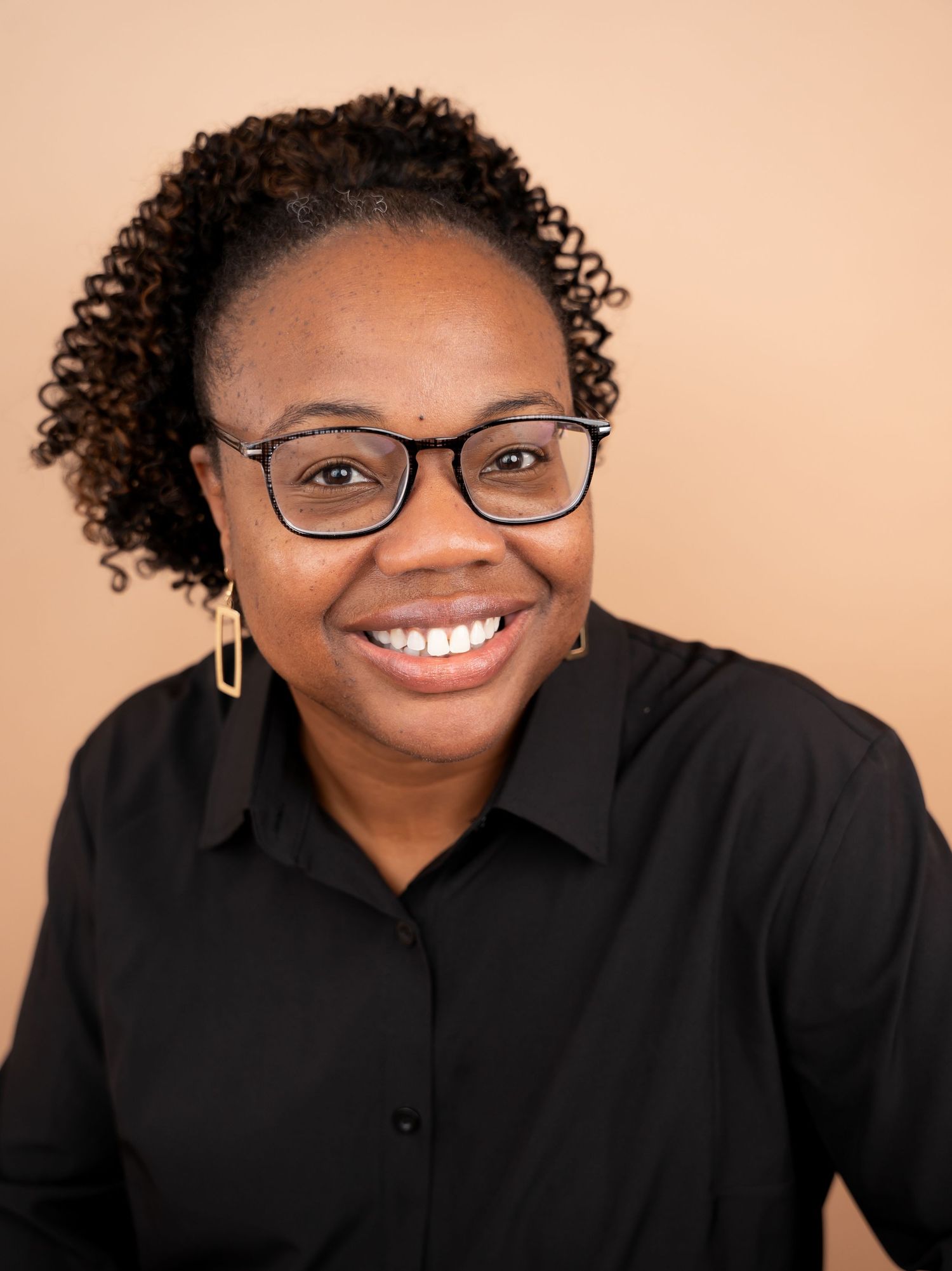 Professional headshots showing person in black top with curly hair and glasses against warm background.