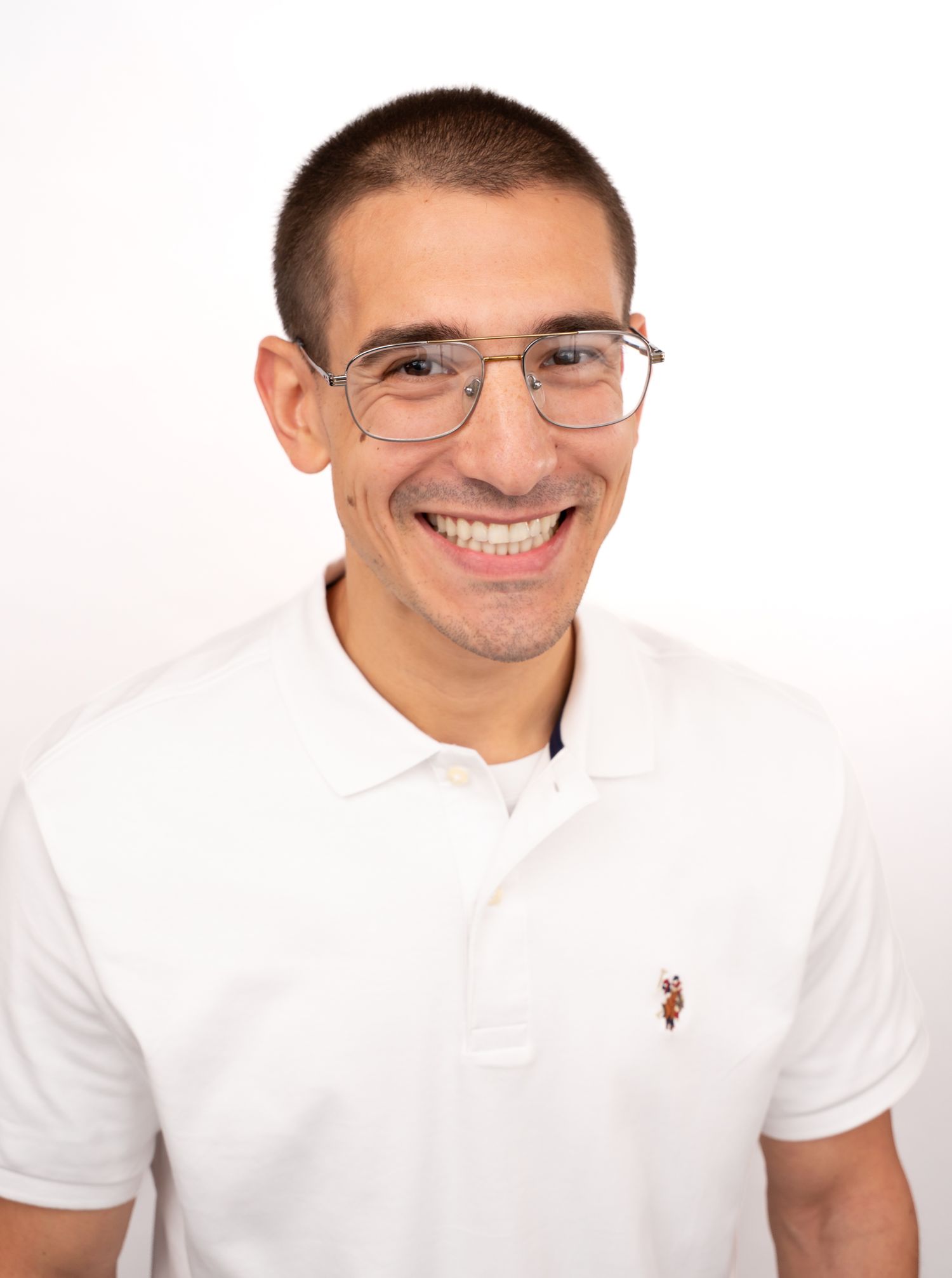 Smiling young man with short hair and glasses wearing a white polo shirt against a white background.
