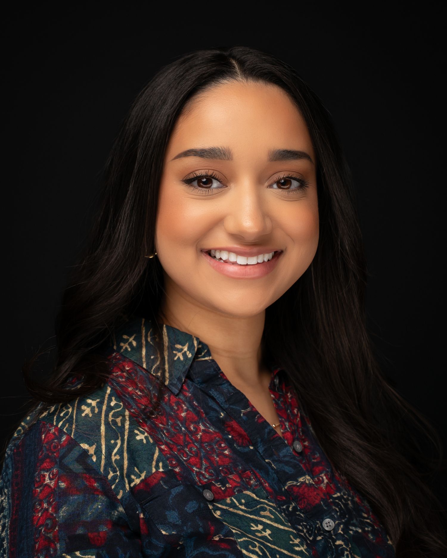 Young woman with long dark hair smiling warmly in a colorful patterned blouse.