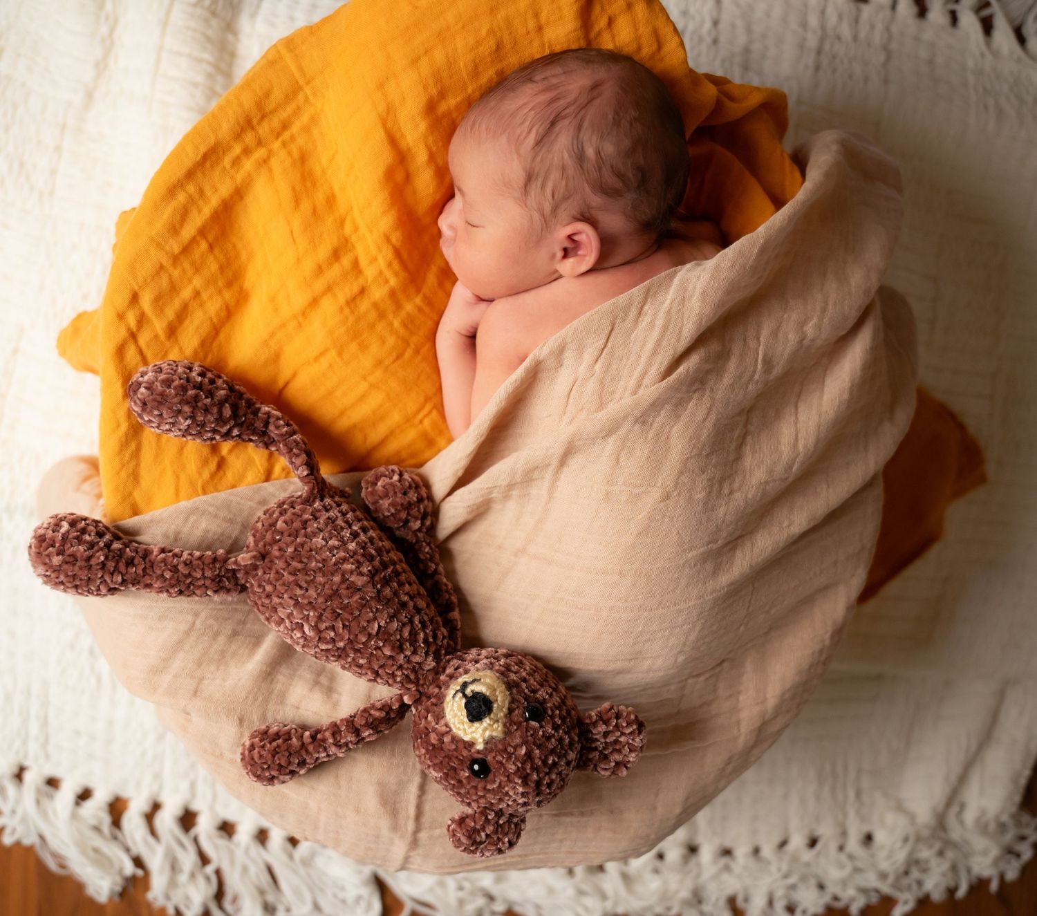 A small brown teddy bear plush toy rests on a cream and orange colored blanket.