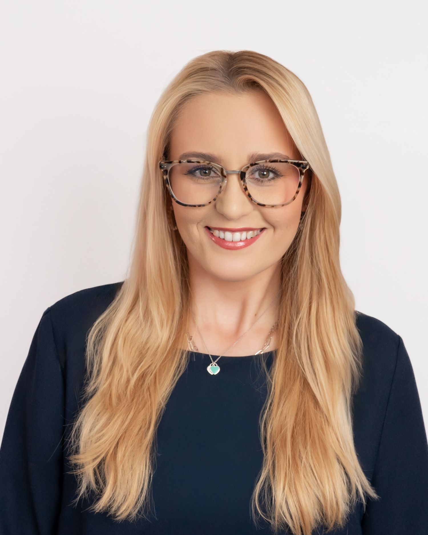 Professional headshot of a blonde woman wearing glasses and a dark top smiling at the camera.