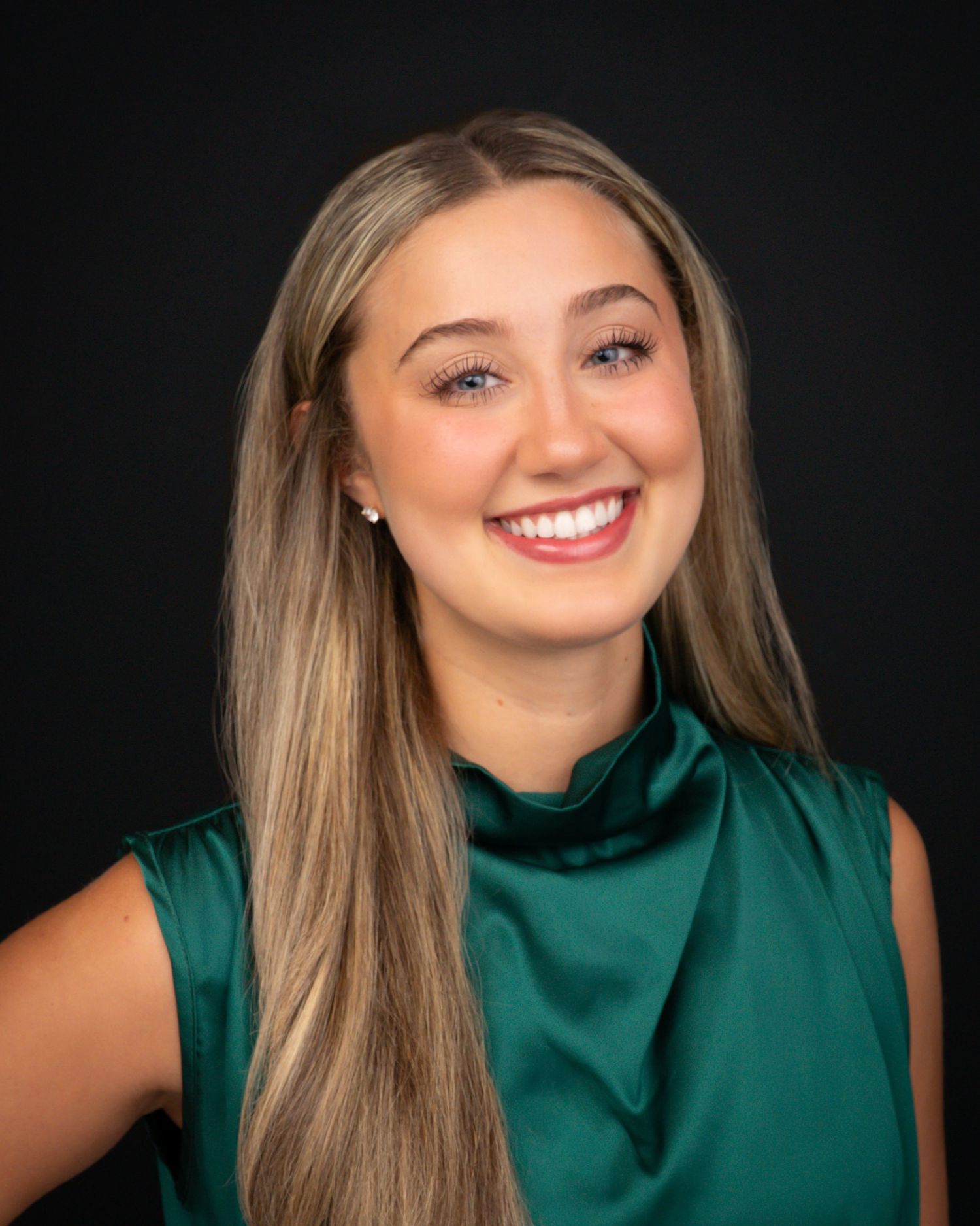 Young woman with long blonde hair smiling brightly in a green satin top.