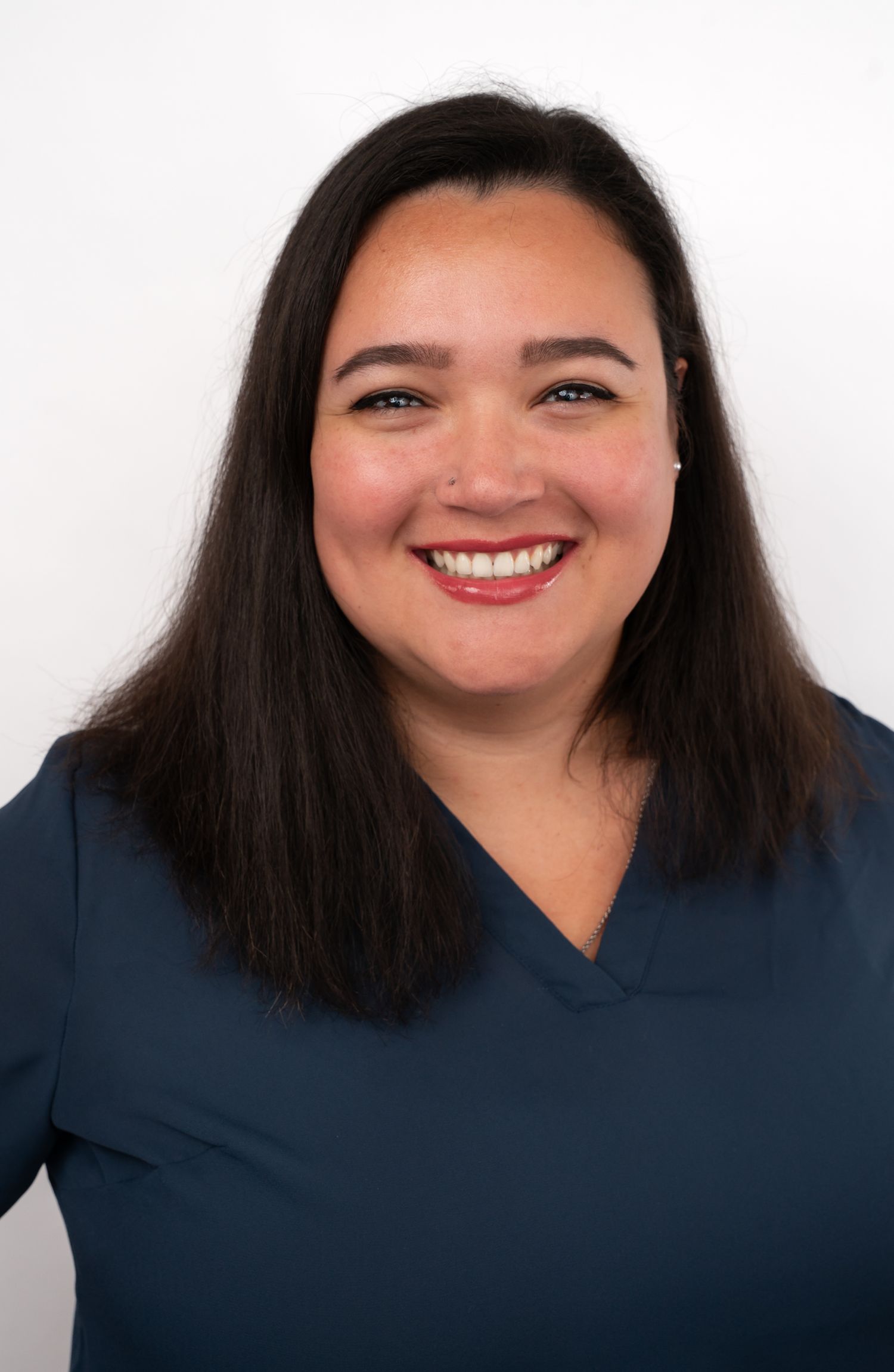 Smiling woman with dark hair wearing a teal scrub top poses for a professional headshot photo.
