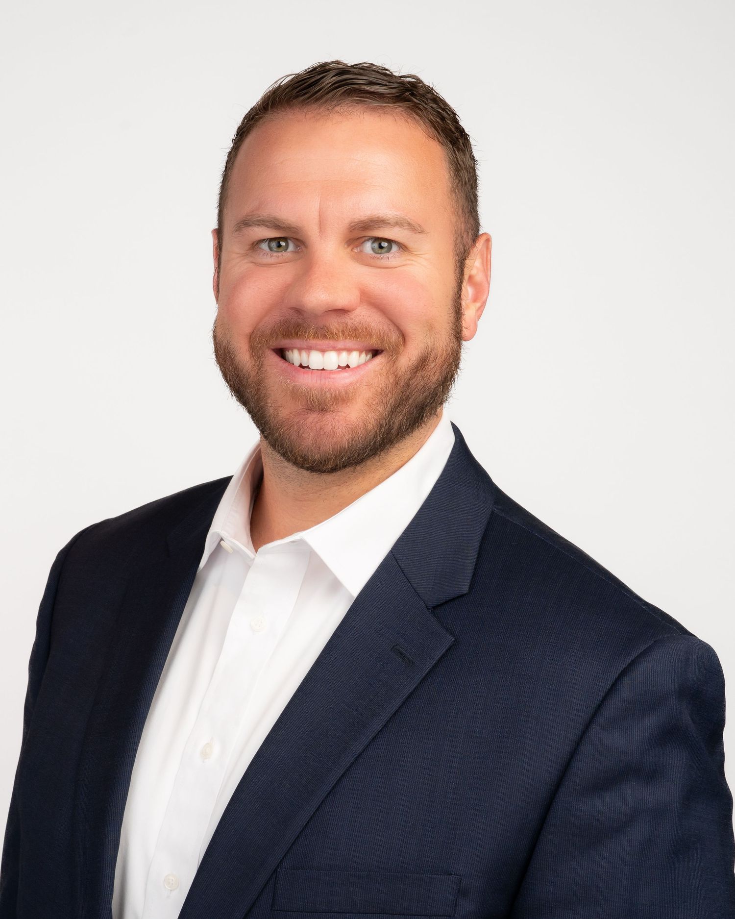 Professional headshot of a smiling man in a navy blazer and white shirt against a light background.