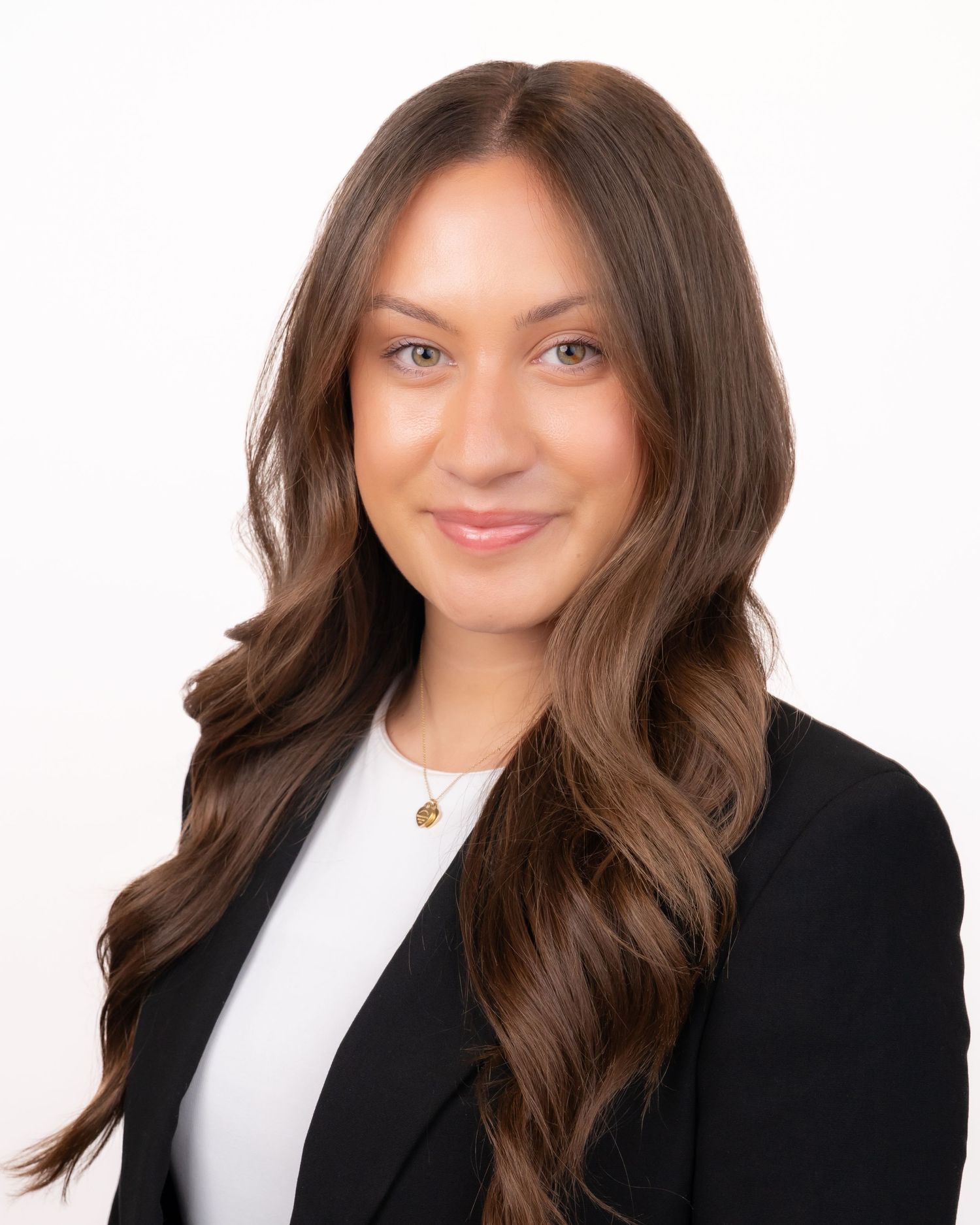 Professional headshot of a young woman with long brown hair wearing a black blazer and white top with a gold necklace.