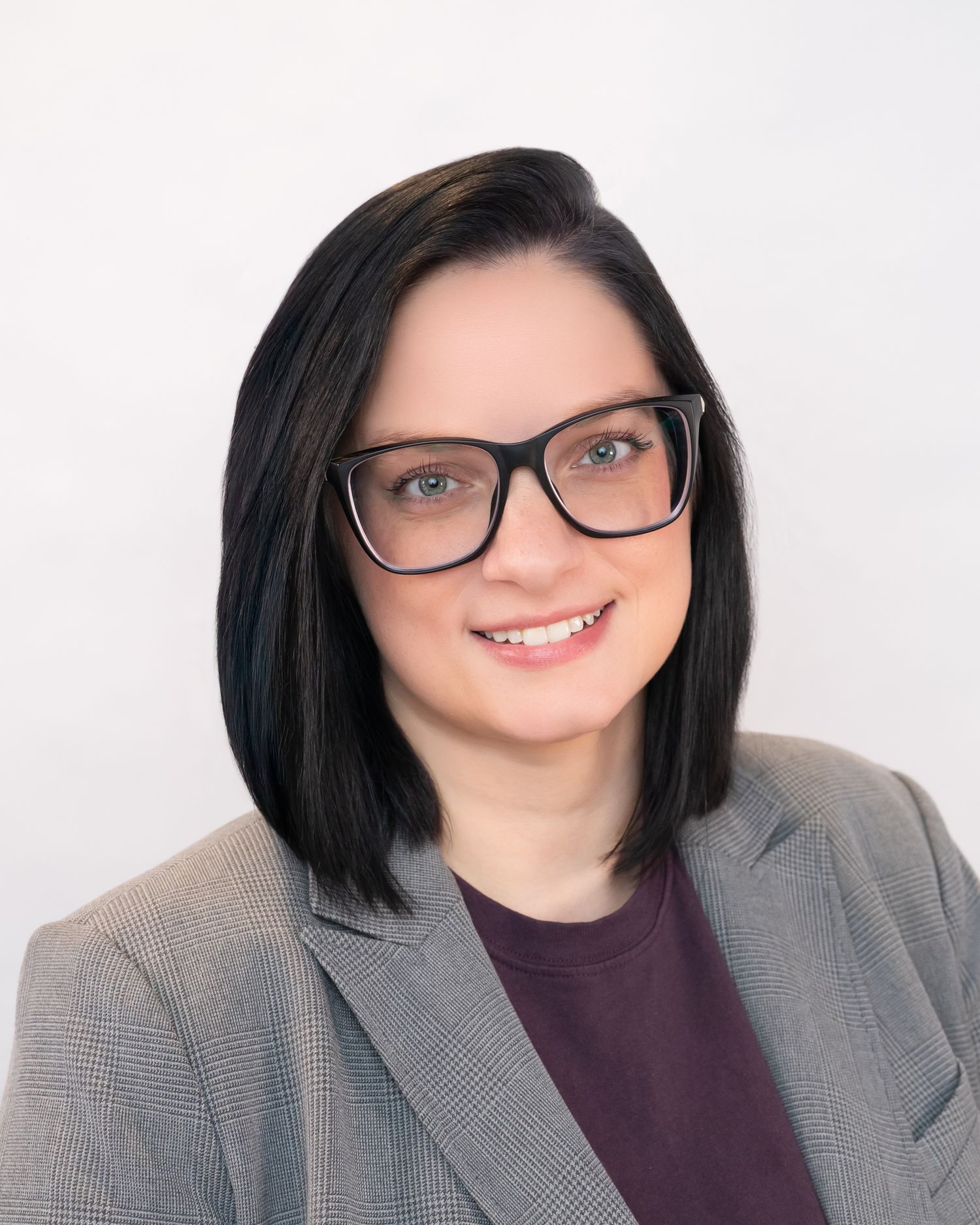 Professional woman with dark bob hair and glasses wearing a gray blazer and purple top, smiling confidently.