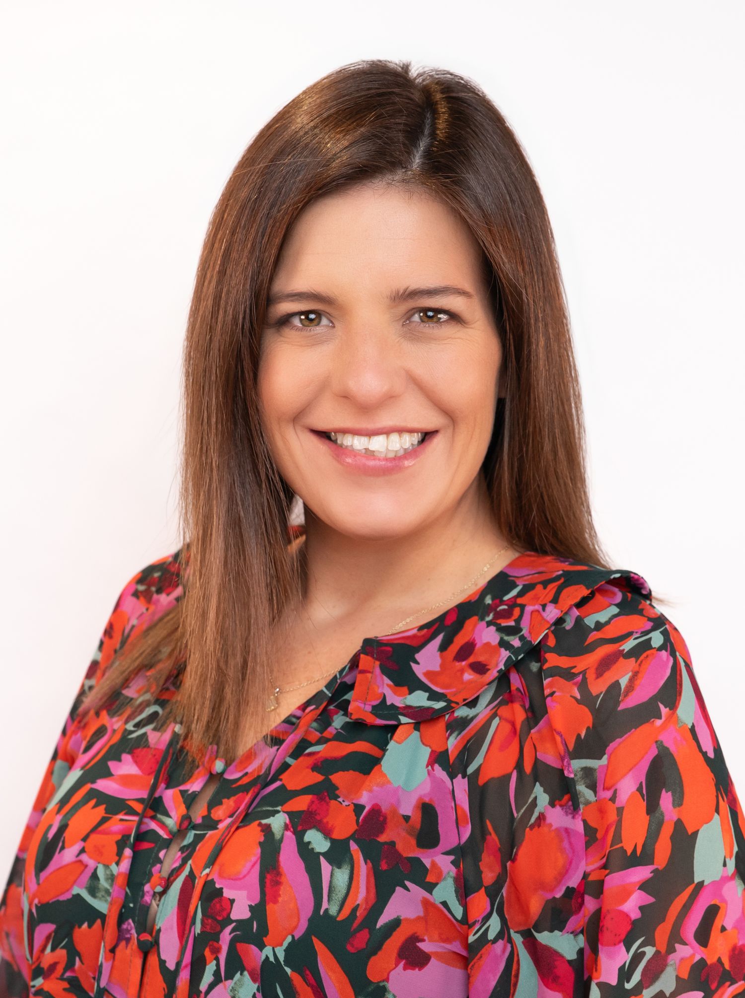 Smiling woman with brown hair wearing a colorful floral blouse poses for a professional headshot photo.
