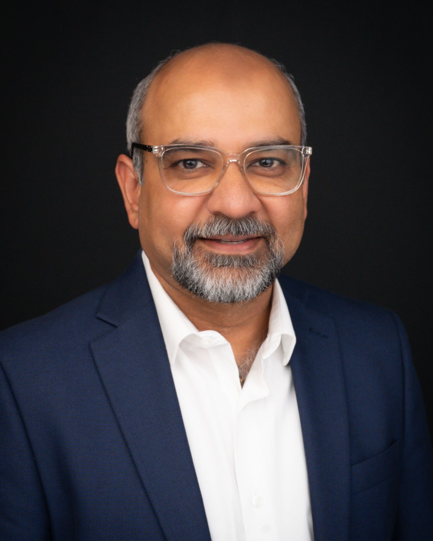 Professional headshot of a middle-aged man with glasses wearing a navy blazer and white shirt.