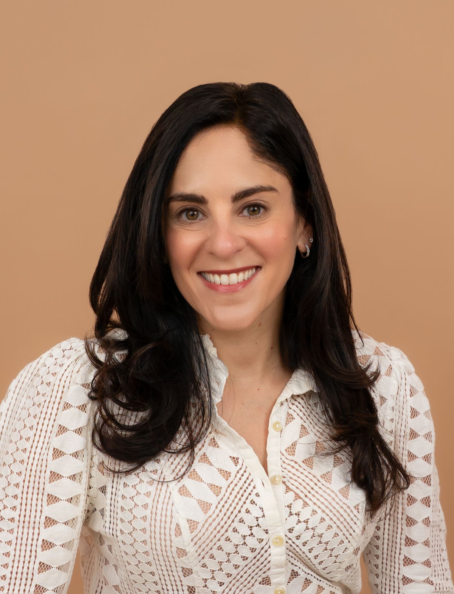 A woman with dark hair wearing a white lace top smiles warmly in a series of four similar portrait poses.