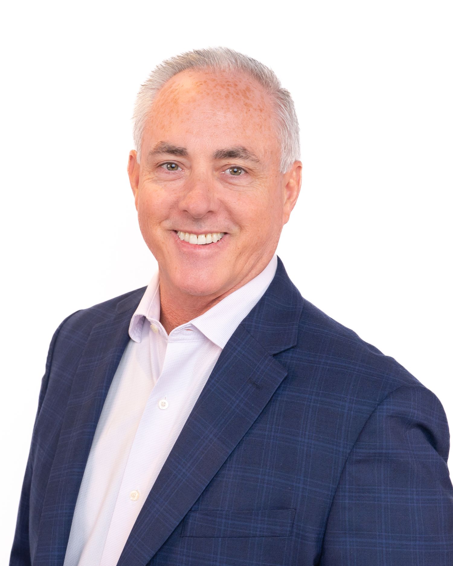 Professional headshot of a smiling middle-aged man with gray hair wearing a navy plaid blazer and white dress shirt.