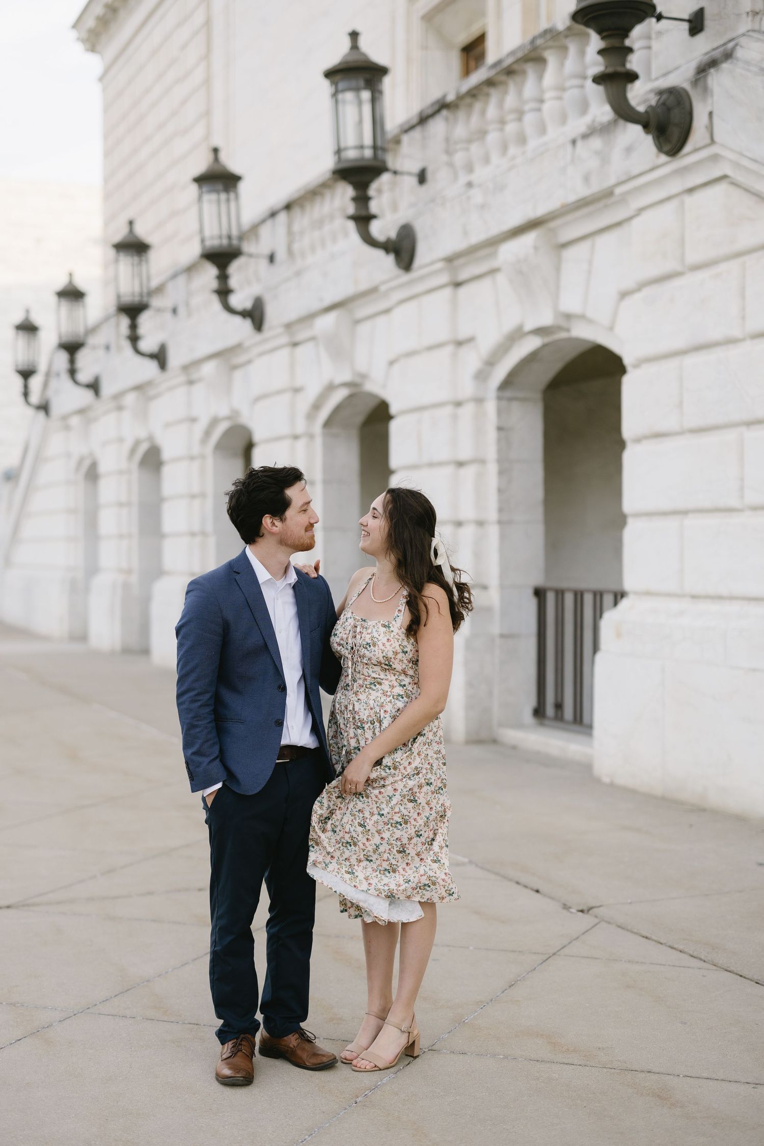 Romantic couple shares tender moments along white stone colonnade with vintage lanterns at historic building.